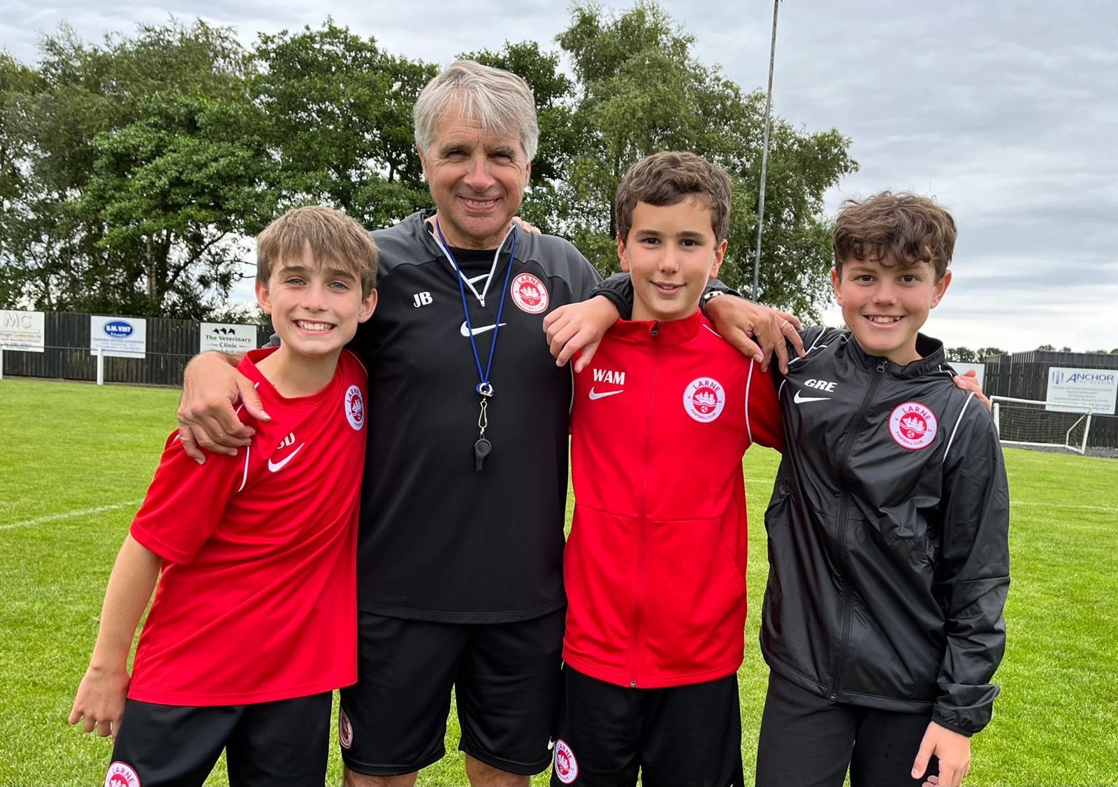 Coach with three young soccer players, all in red shirts, on a grassy field.