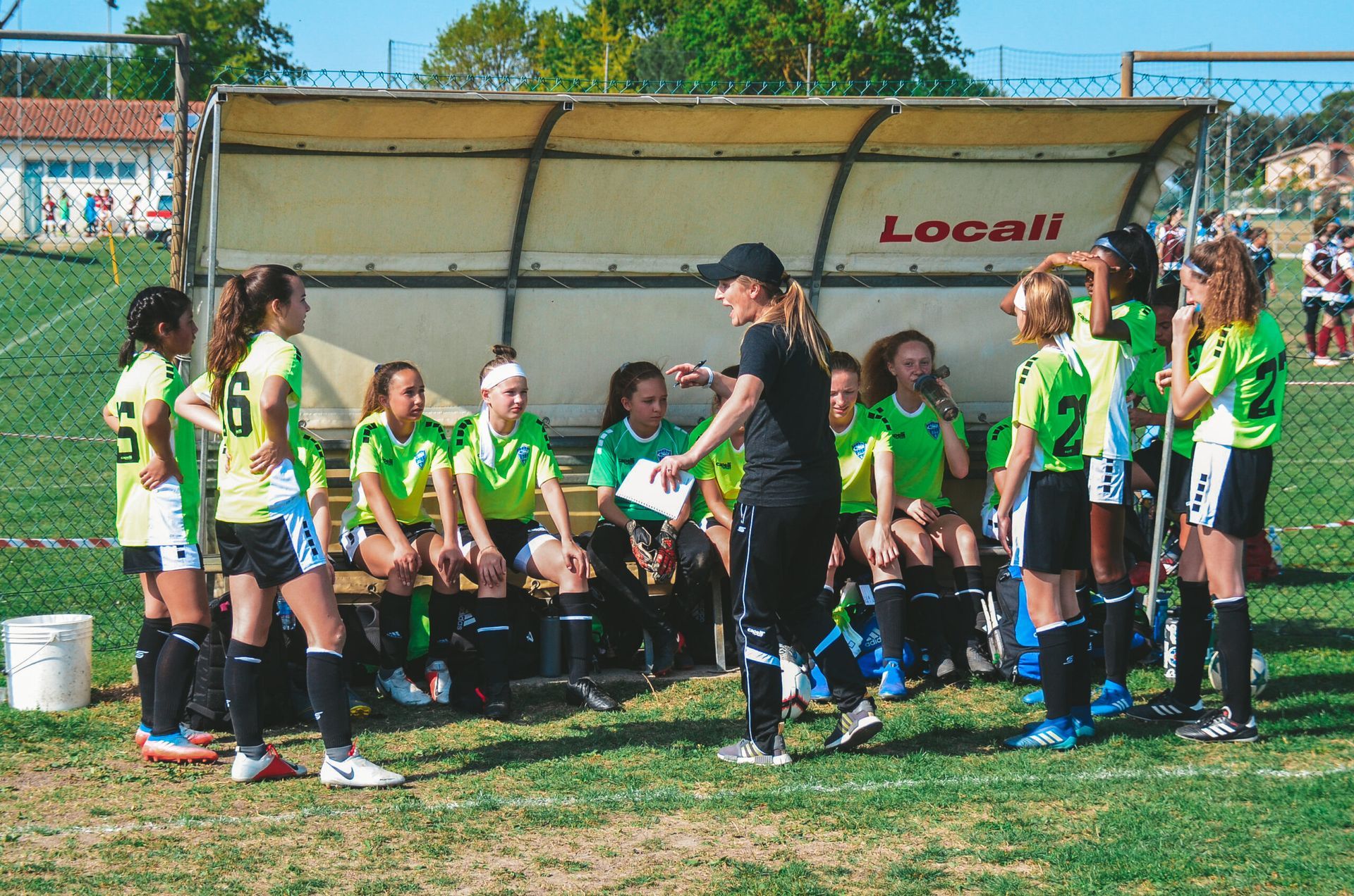 Soccer team in lime green jerseys listens to a coach on the sidelines during a game.