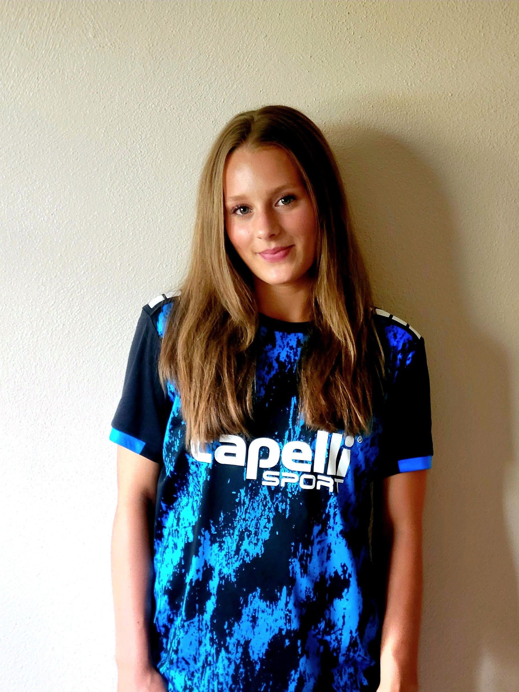 Woman in blue and black sports shirt stands in front of a neutral wall.