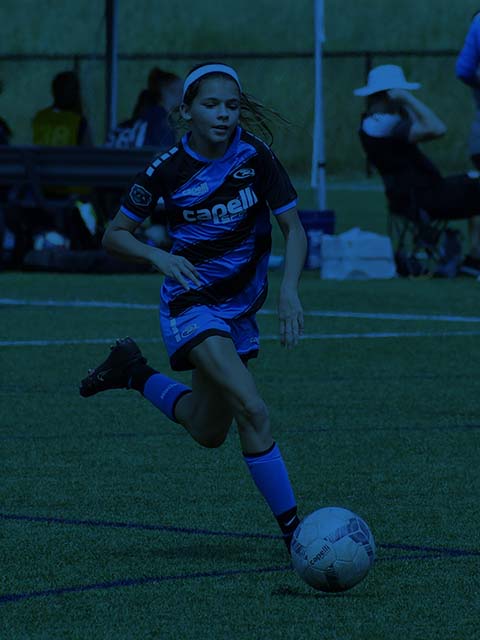 Soccer player in blue uniform dribbling a soccer ball on a field.