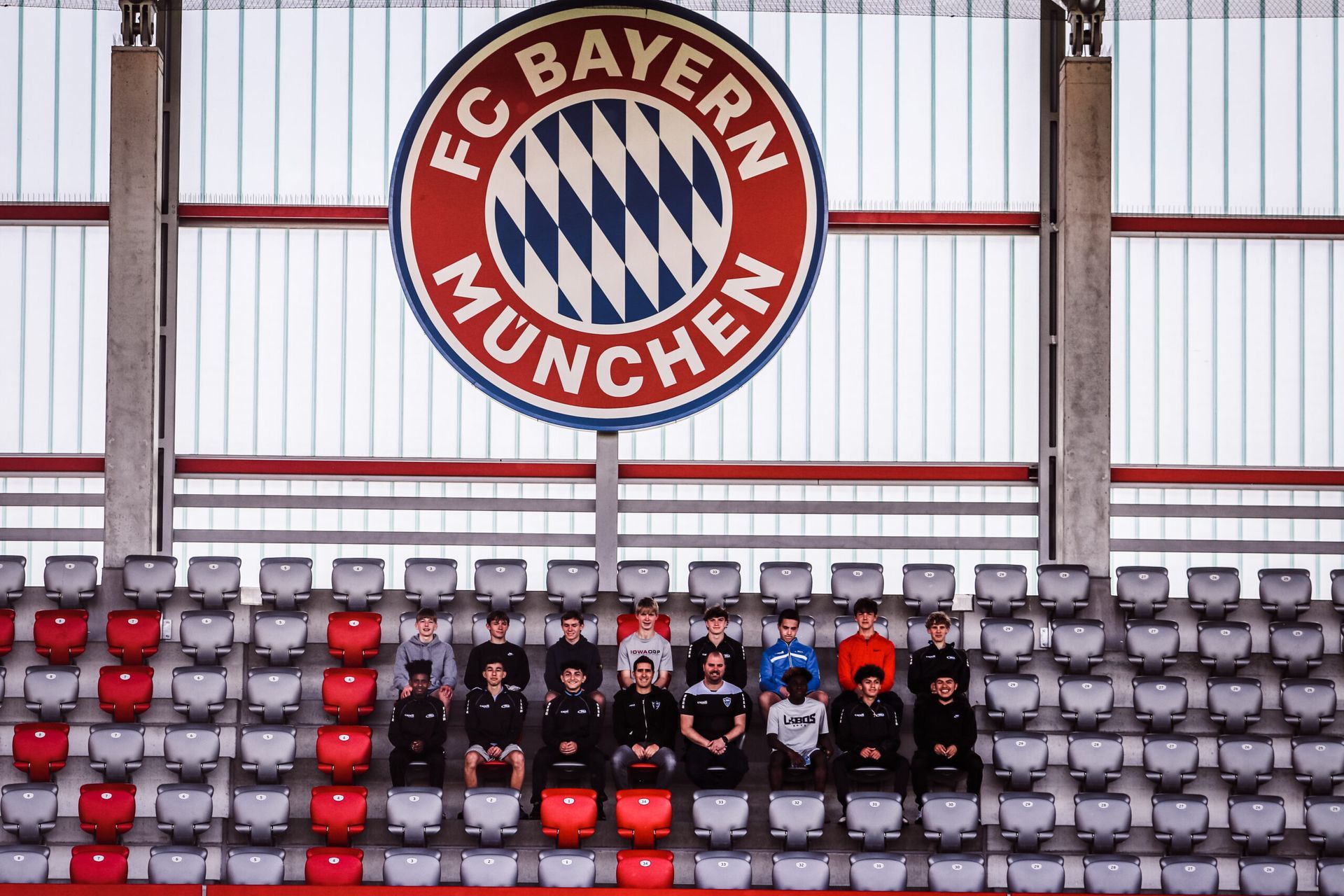 Group of people sitting in stadium seats under an FC Bayern Munich logo.