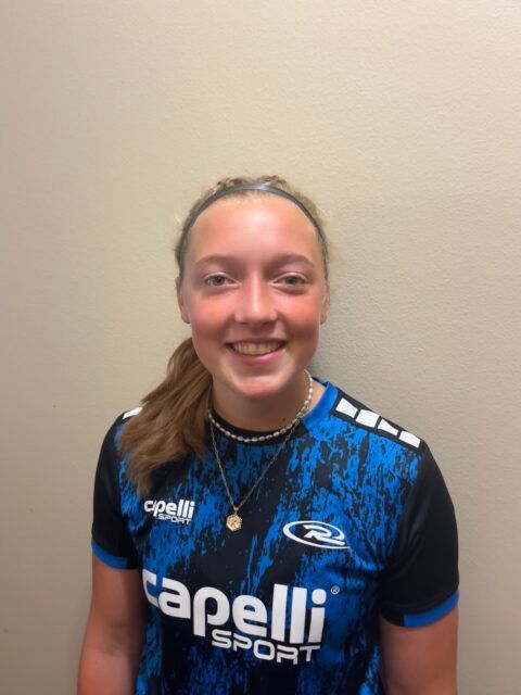 Woman wearing a blue and black sports shirt smiles at the camera, light background.