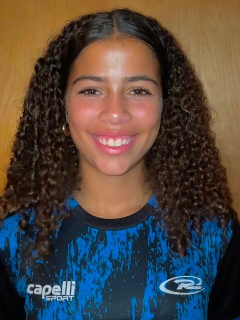 Young person with curly brown hair, smiling, wearing a blue sports shirt.