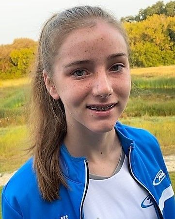 Teen girl with braces wearing a blue and white jacket, smiling, outdoors.