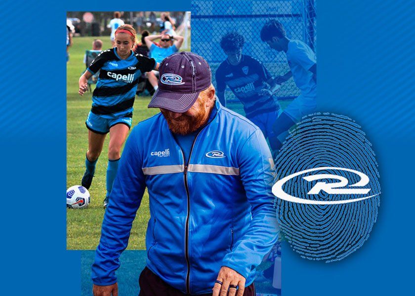 Soccer coach wearing blue jacket with players in background.