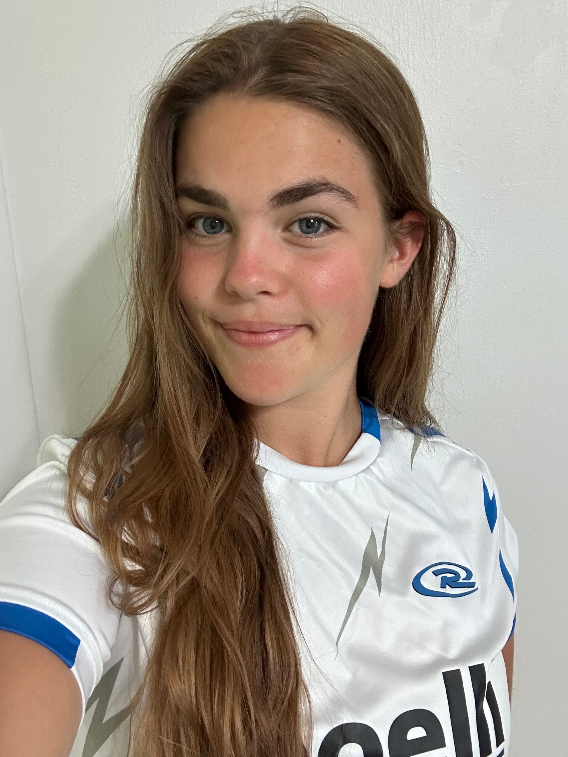 Woman with long brown hair wearing a white and blue athletic shirt, smiling at the camera.