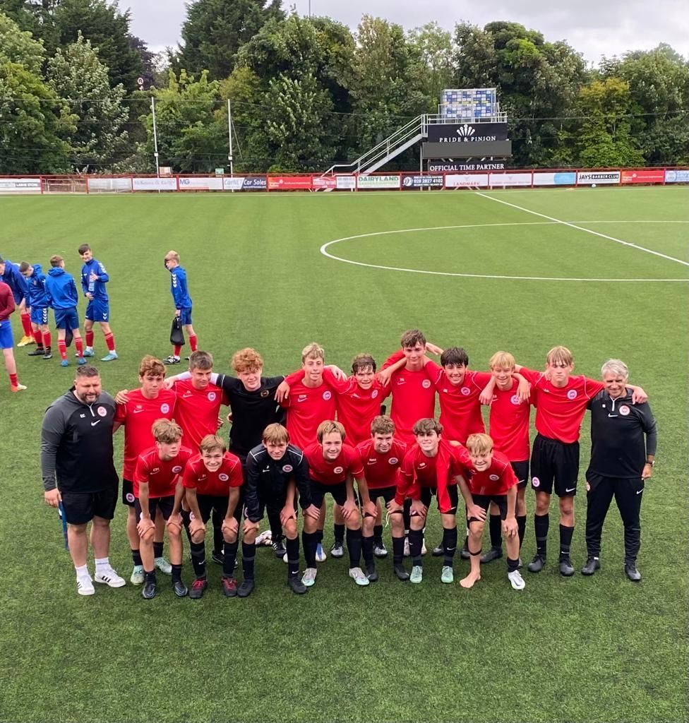 Soccer team in red shirts and black shorts posing on a field with coaches.