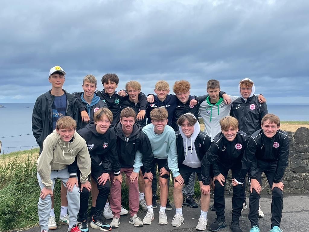 Group of teenagers posing outdoors near ocean, cloudy sky.