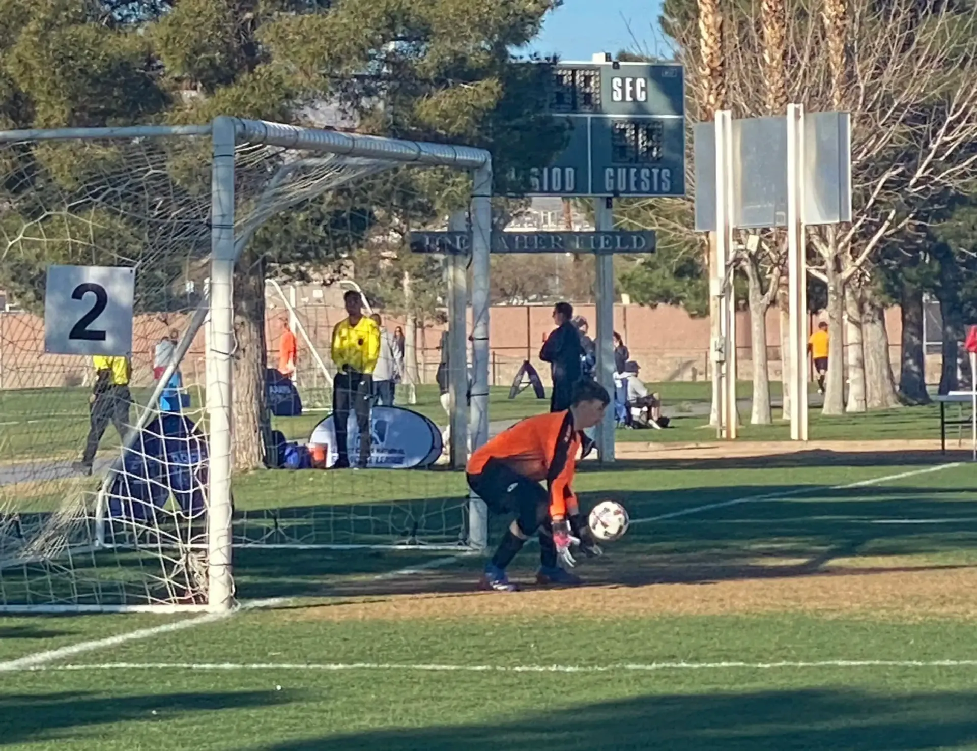 Soccer goalie in orange preparing to catch the ball in front of the goal during a game.