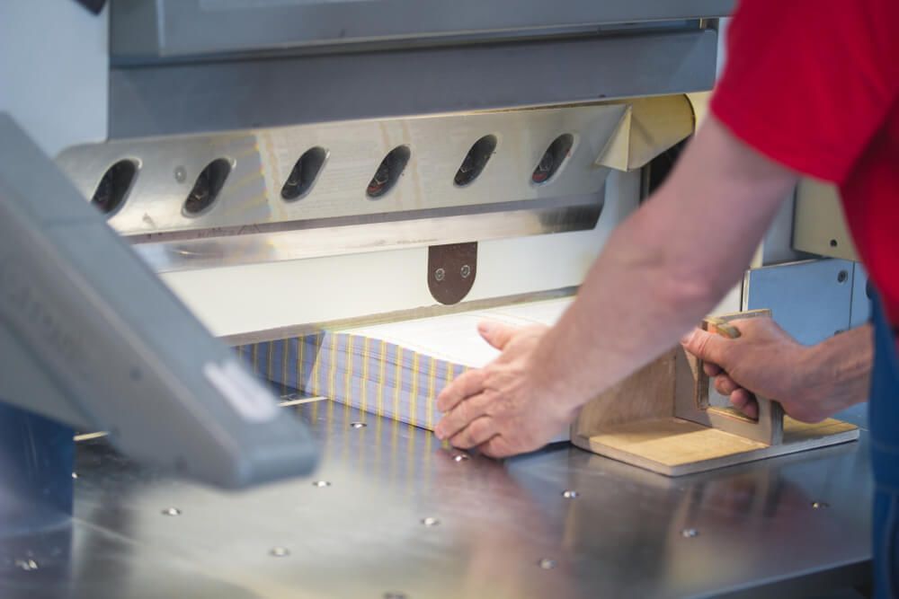 A Person is Cutting a Piece of Paper With a Machine — Aldine Printers in Bungalow, QLD