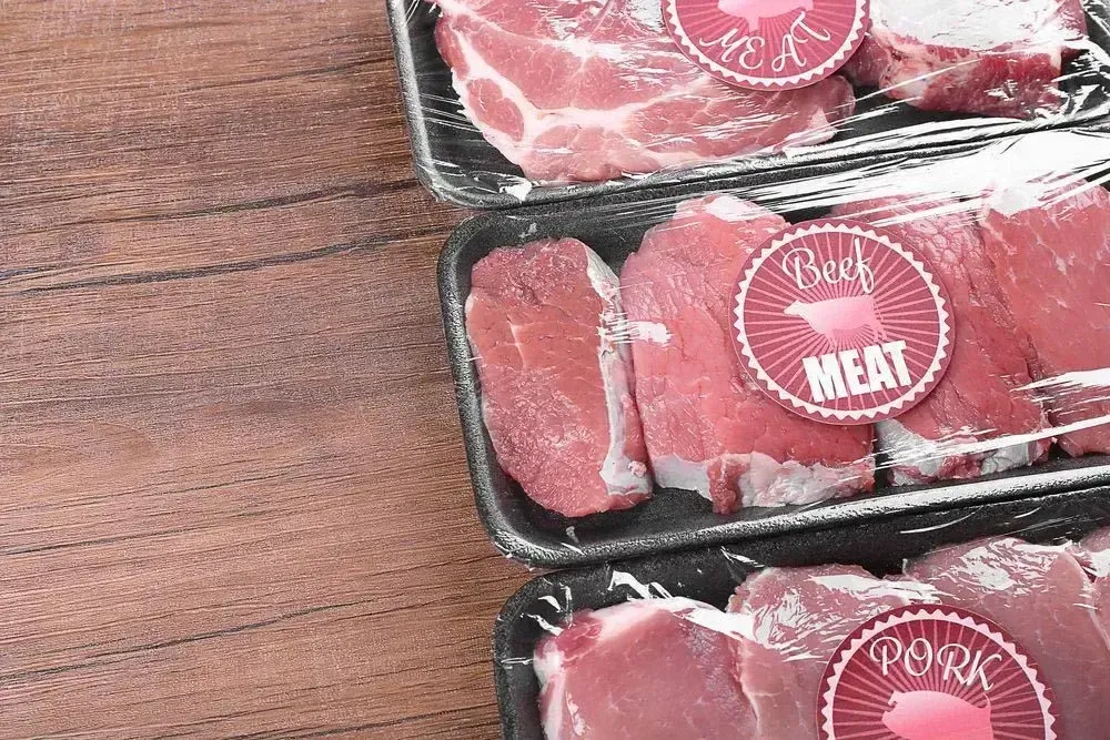 Three packages of red meat on a wooden table. Each package has a round red label with 'beef meat'.