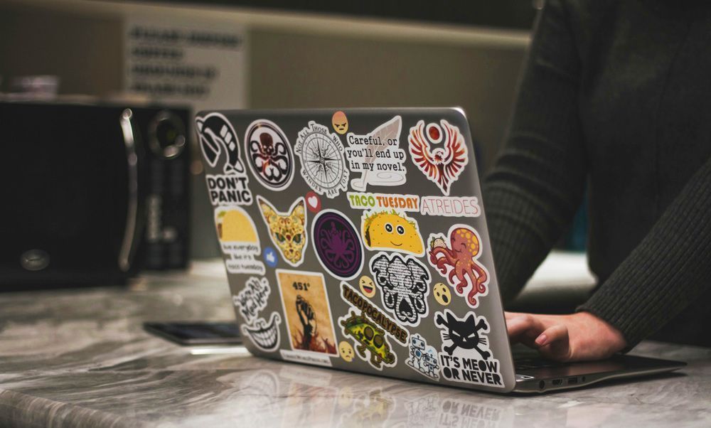 person using laptop covered in colourful custom stickers, showcasing creative sticker design ideas