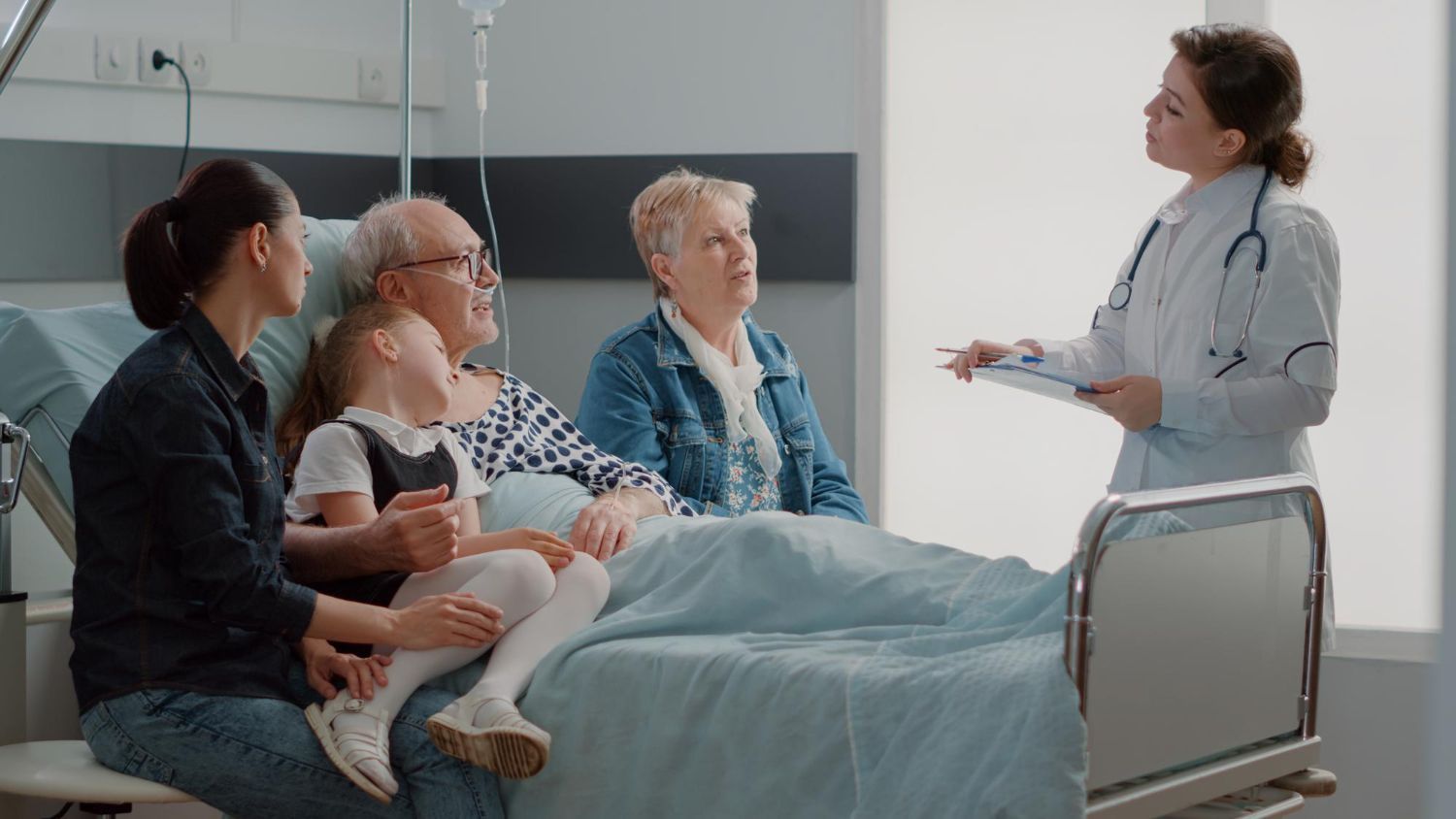 Doctor talking to family at a hospital bedside. Elderly patient in bed, family sitting with them.