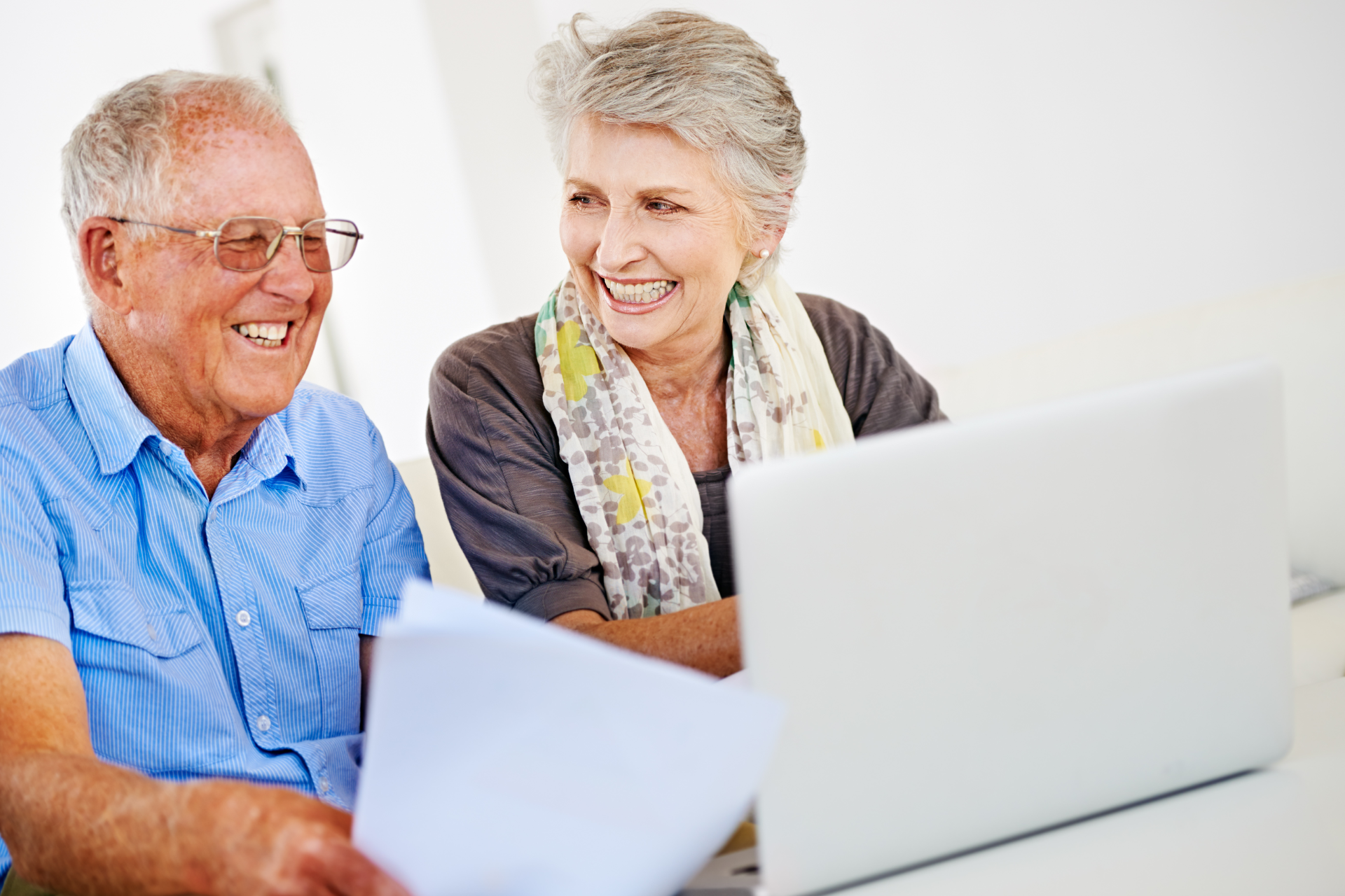 Smiling senior couple looking at laptop, holding documents indoors.