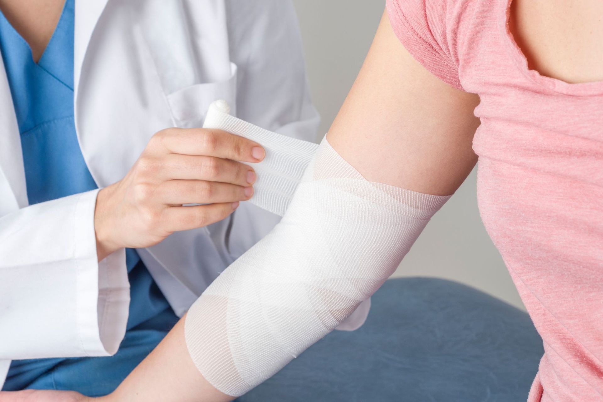 Doctor wrapping bandage around a patient's elbow; inside a medical setting.