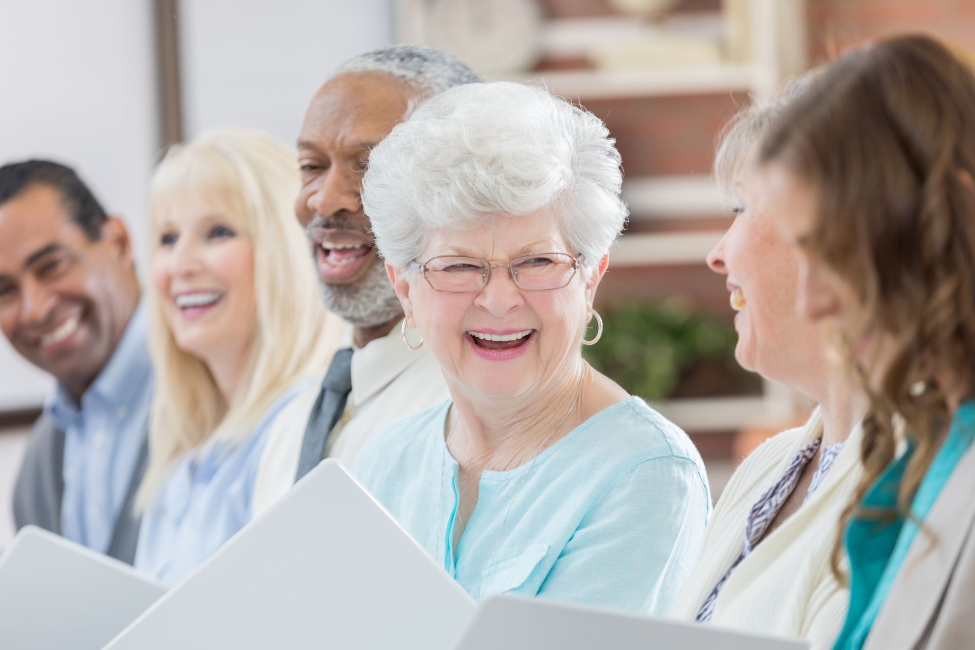 Group of smiling seniors, diverse in race and gender, singing with music books.