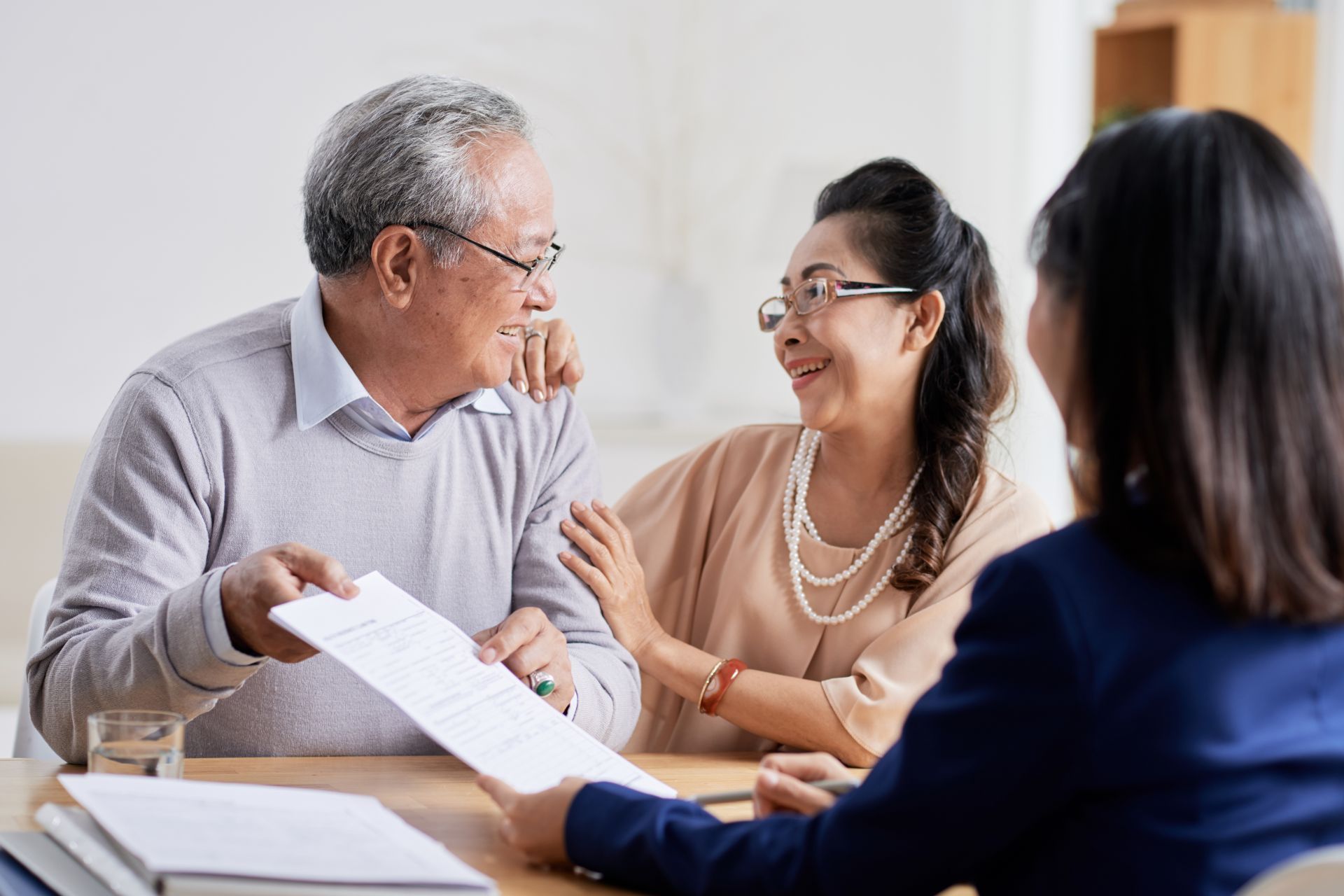 Senior couple reviewing paperwork with a financial advisor at a table; they are smiling.