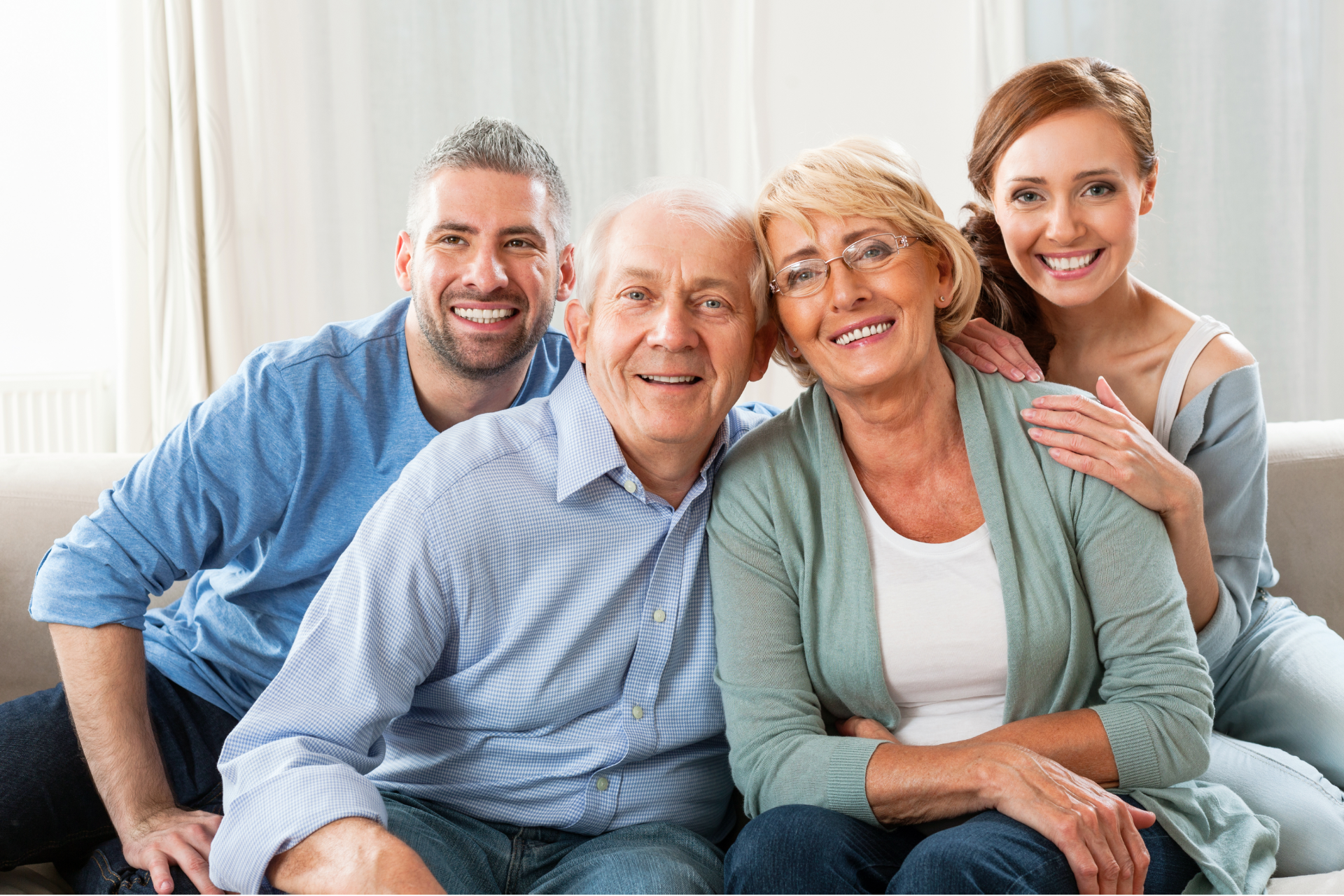 Family of four smiling together on a couch: two older adults with younger couple.