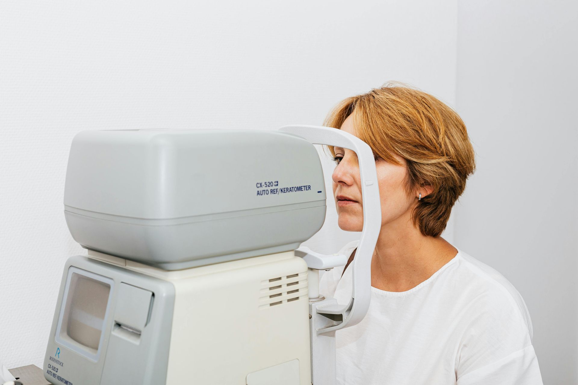 Woman having an eye exam with a medical machine in a white room.