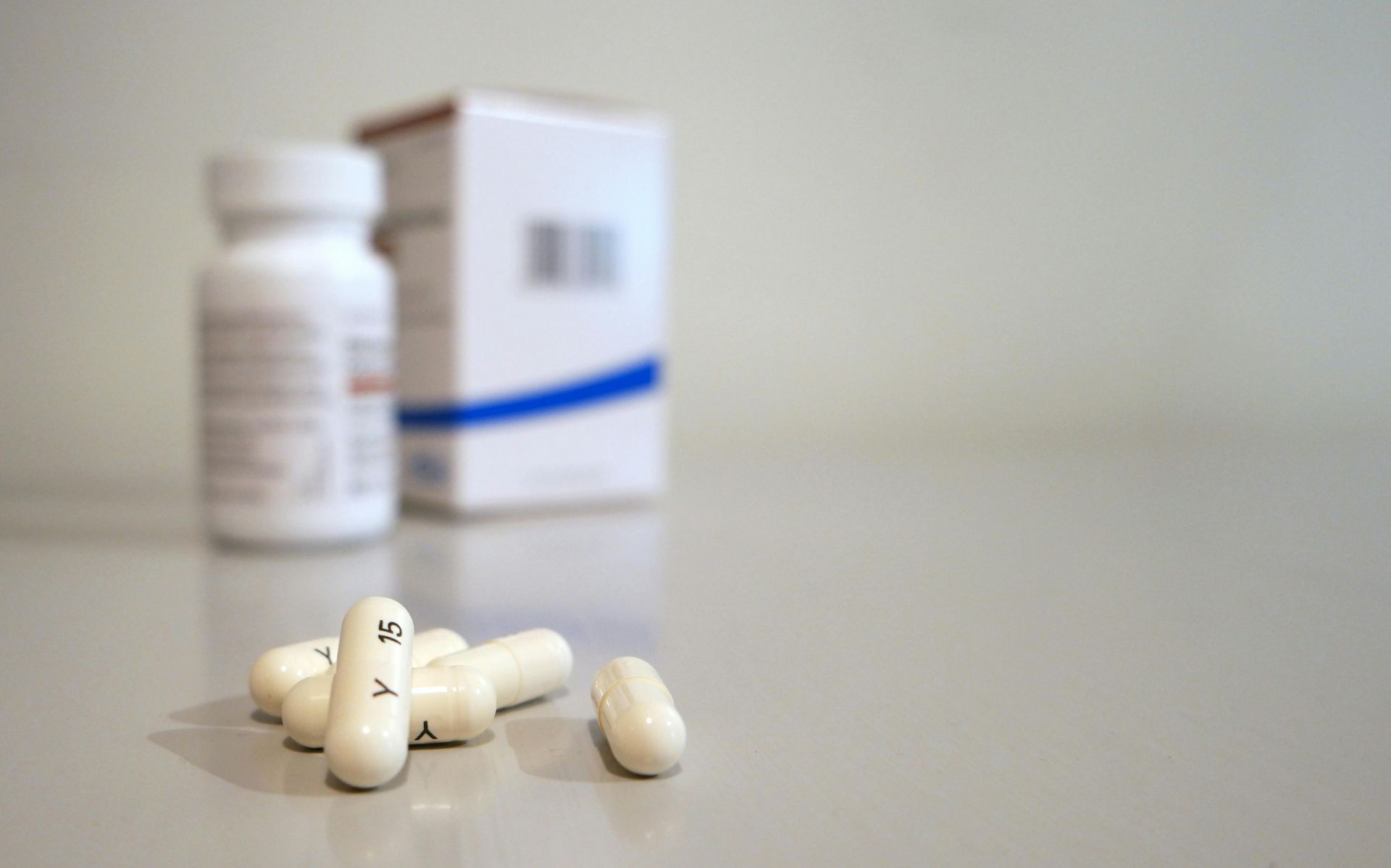 White capsules spilled on a surface, with a white pill bottle and box in the background.