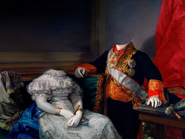 Two headless figures in formal attire pose near a table and a red drape.