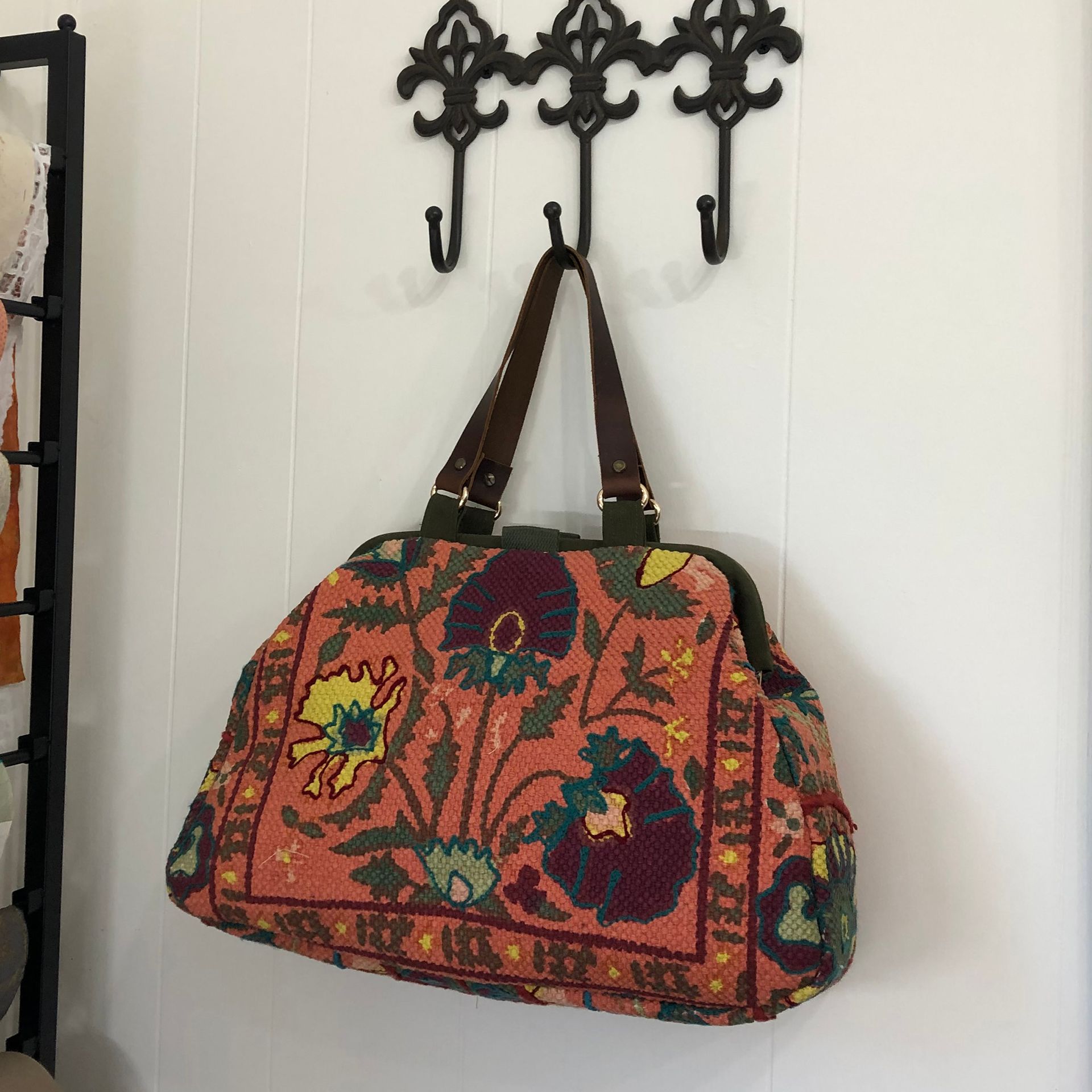 Orange floral tote bag hanging on a black metal hook on a white wall.