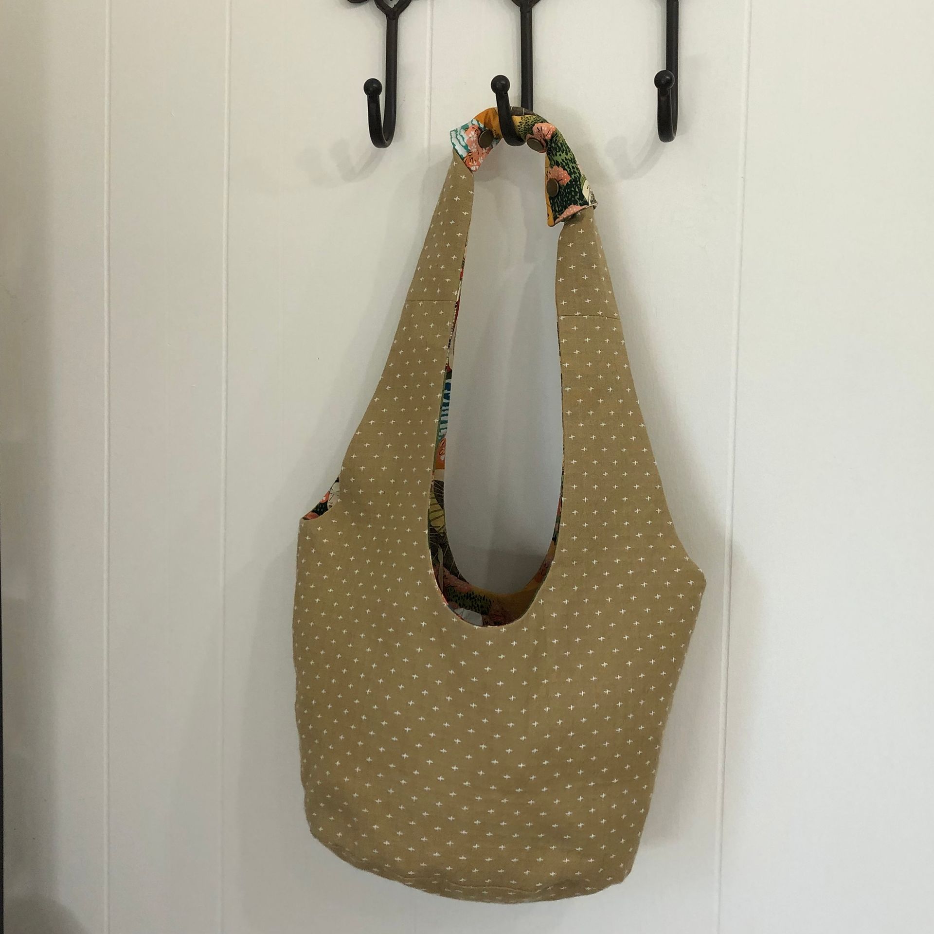 Tan and patterned fabric tote bag, open and resting on a white bedspread.