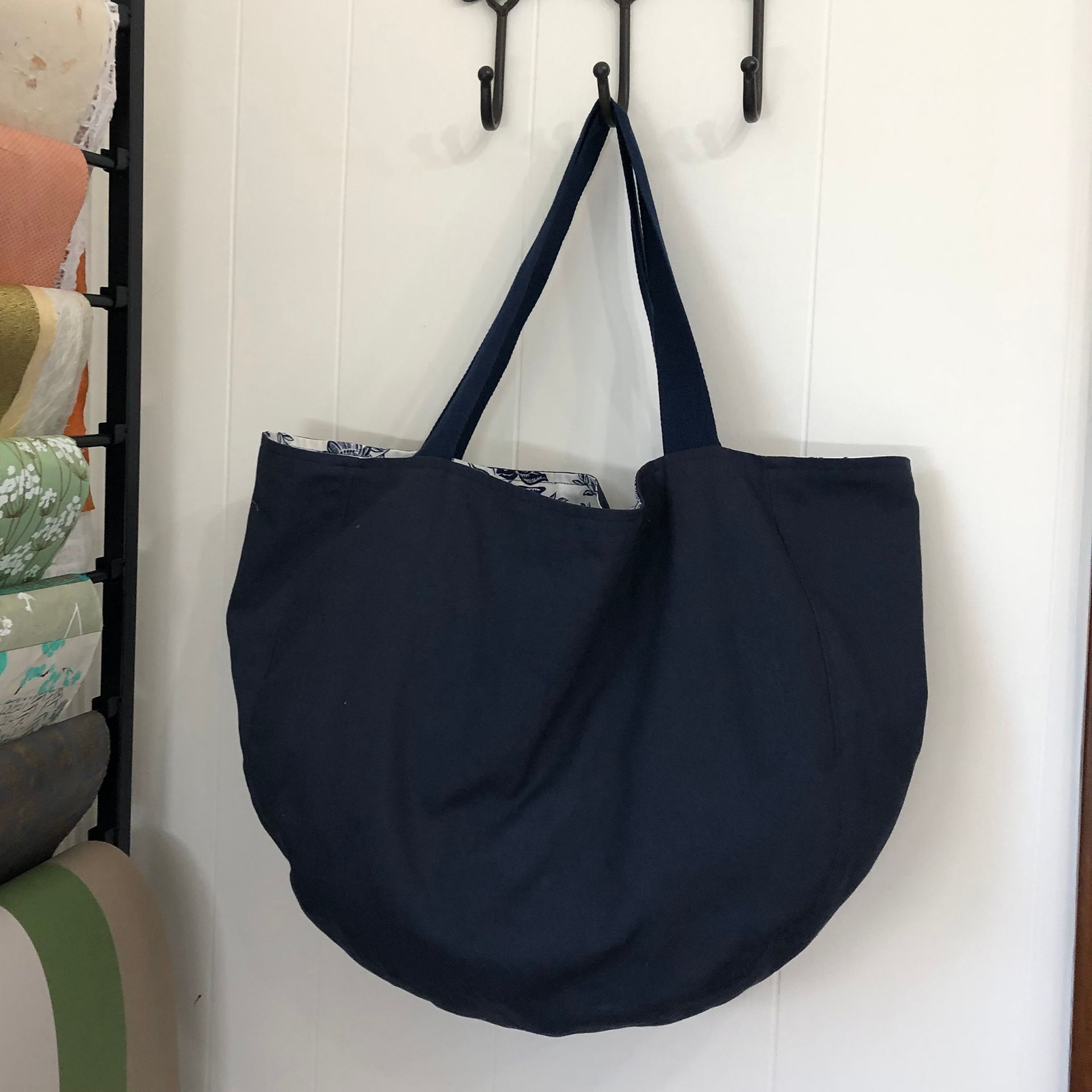Navy blue tote bag hanging on a white wall.