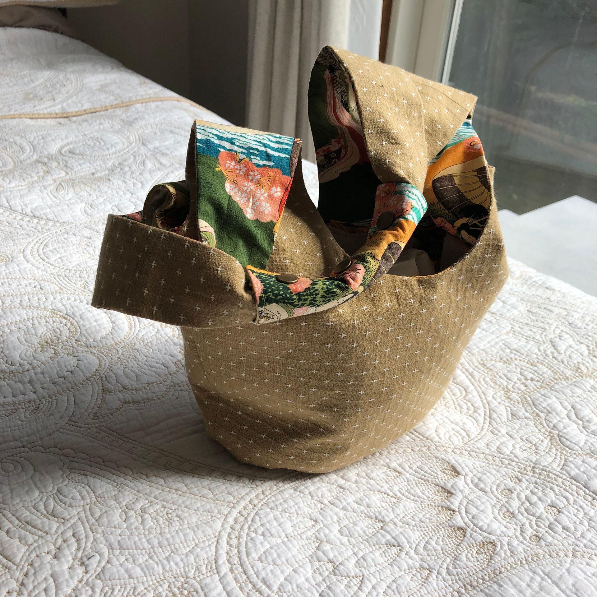 Tan and patterned fabric tote bag, open and resting on a white bedspread.