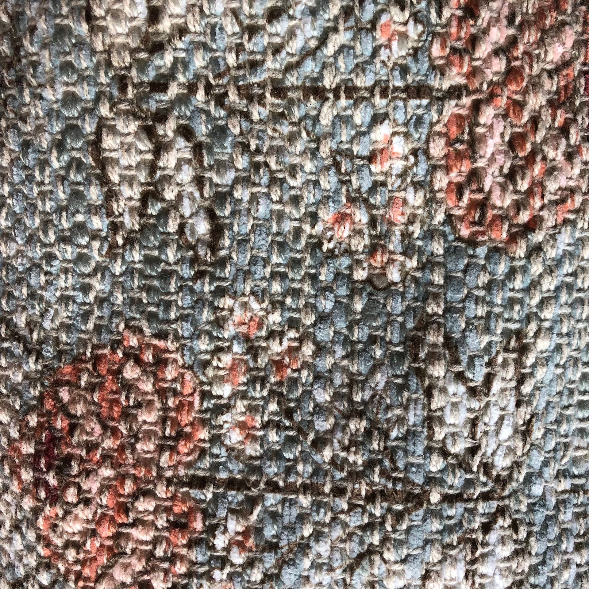 Floral patterned duffel bag hanging on a wall with ornate hooks, next to fabric rolls.