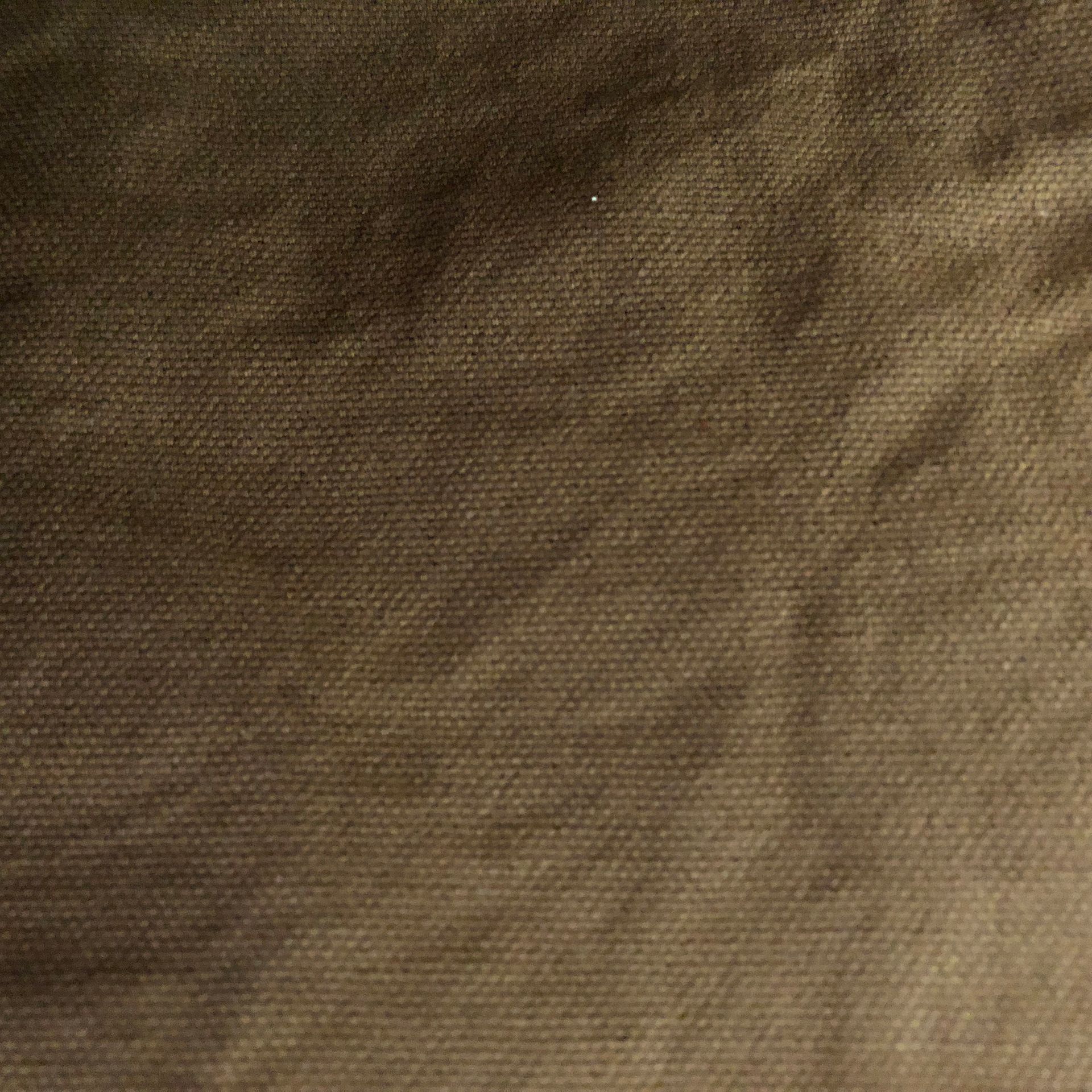 Brown tote bag hanging on a white wall with black hooks. Stacks of fabric are visible on the left.