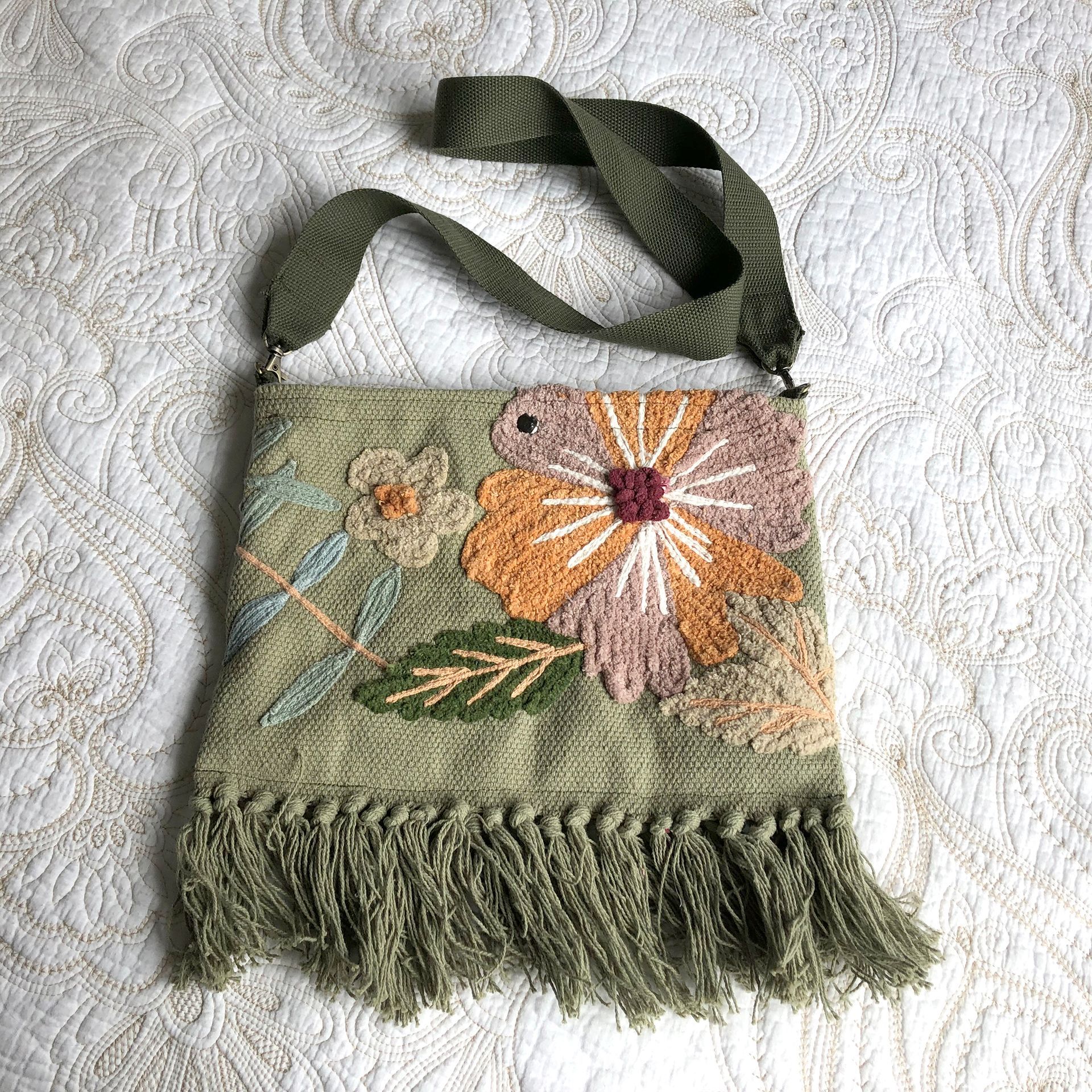 Green textile tote bag with embroidered flowers, fringed bottom and olive straps.
