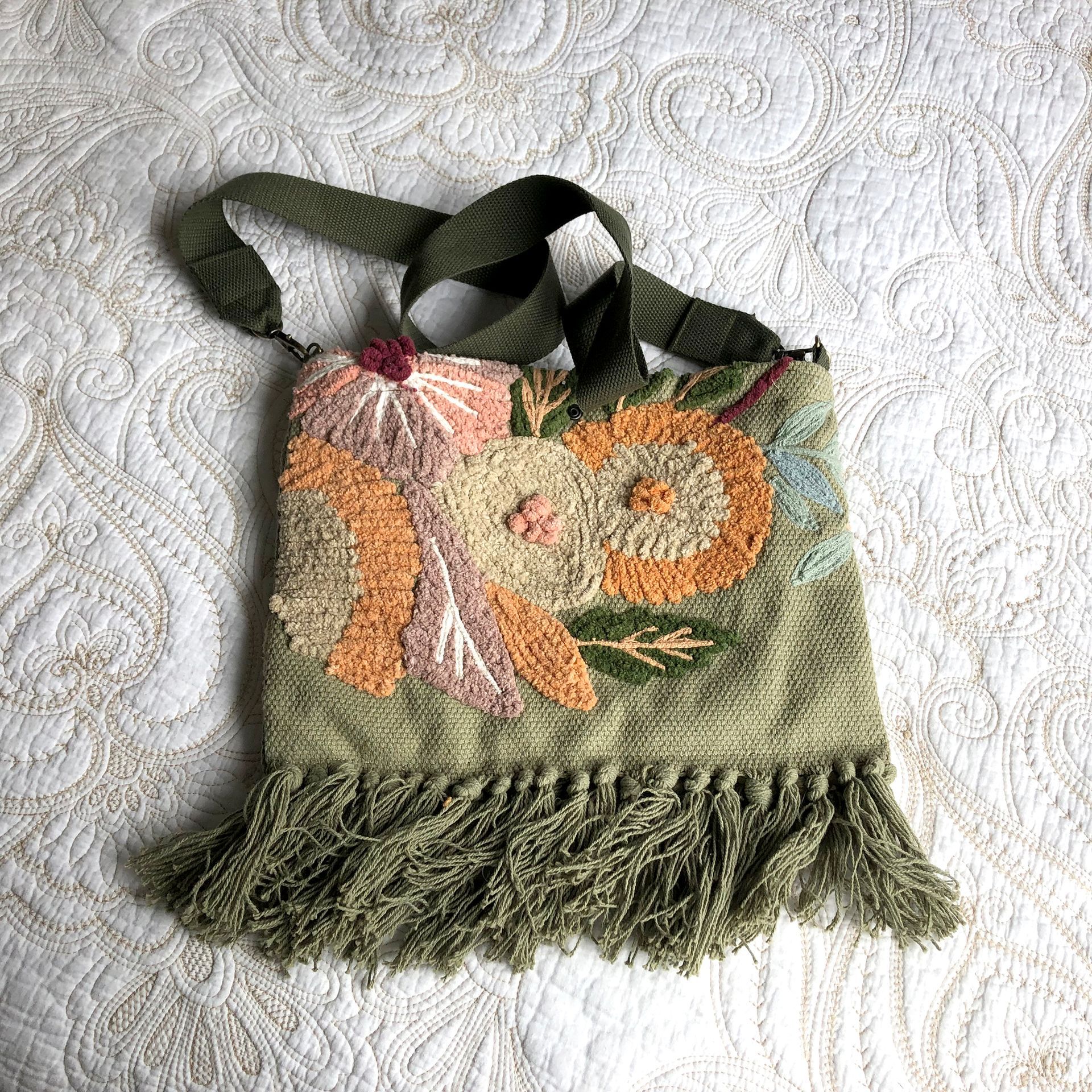 Green textile tote bag with embroidered flowers, fringed bottom and olive straps.