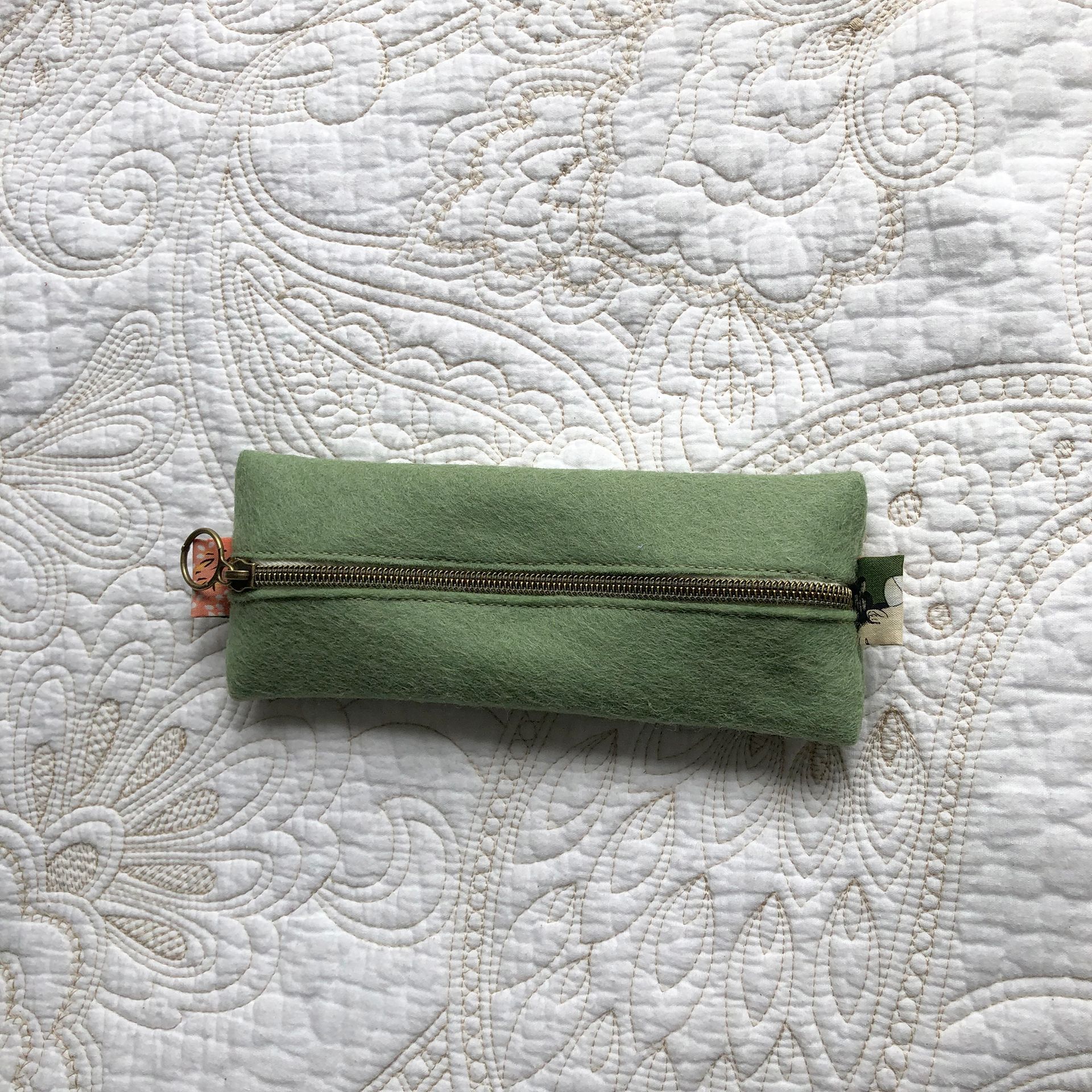 Green fabric zippered pouch on a patterned white surface.