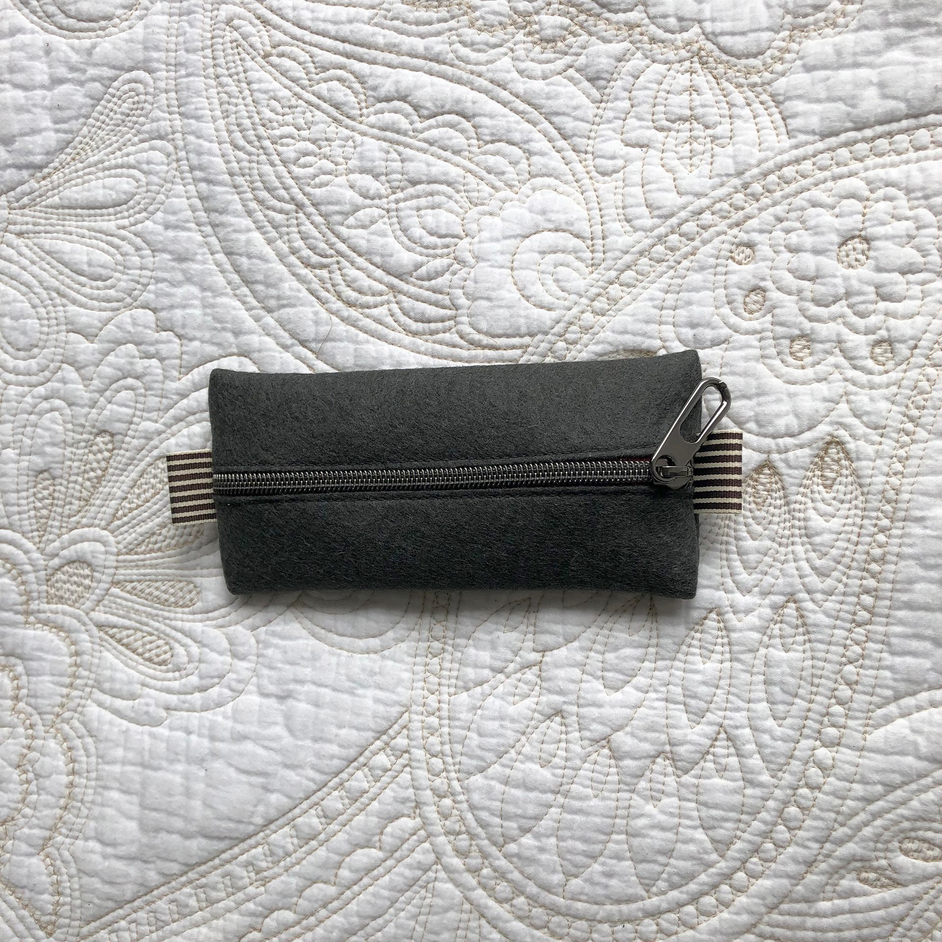 Dark gray zippered pouch with tan and brown striped accent on a patterned white surface.