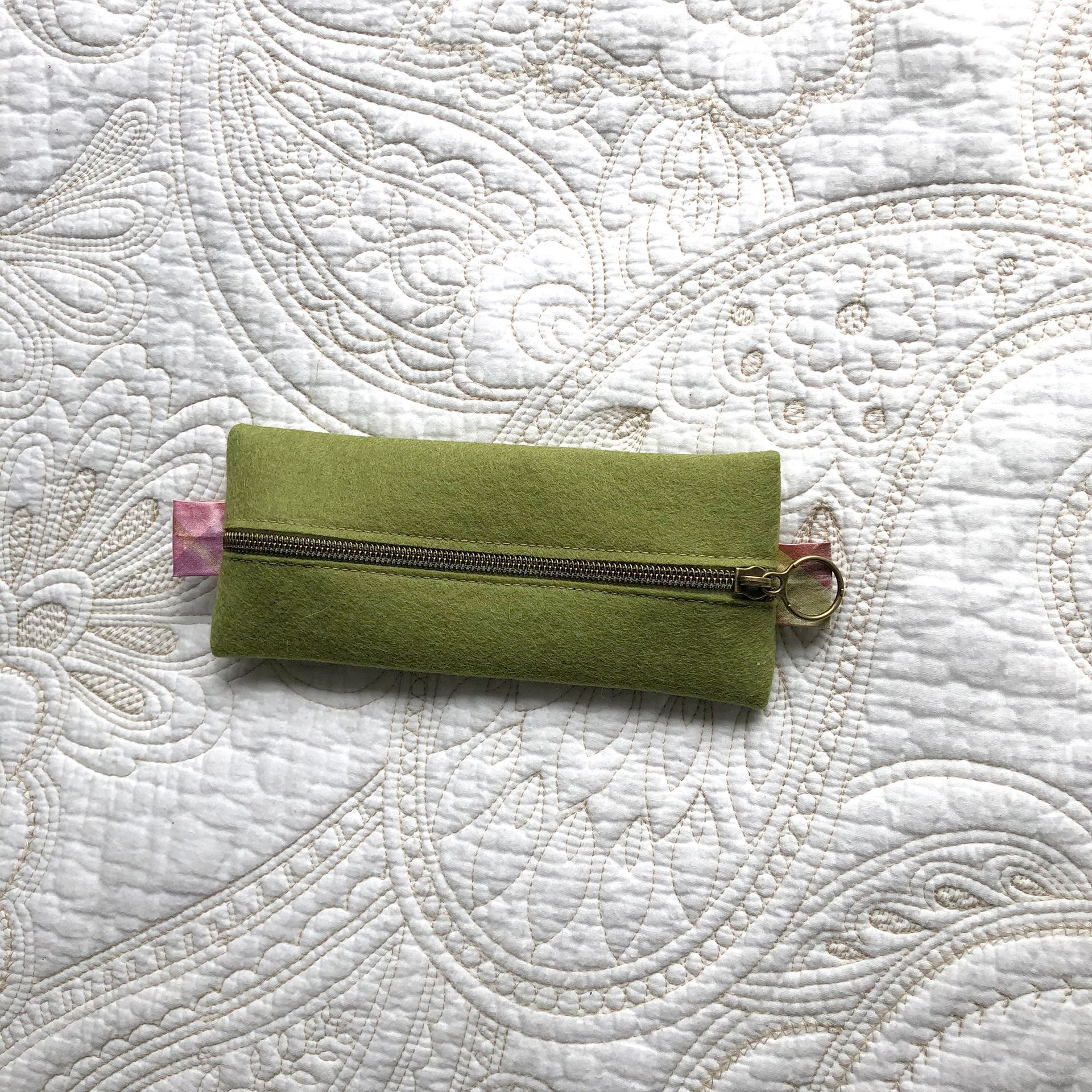 Green suede key case on white quilted bedspread.