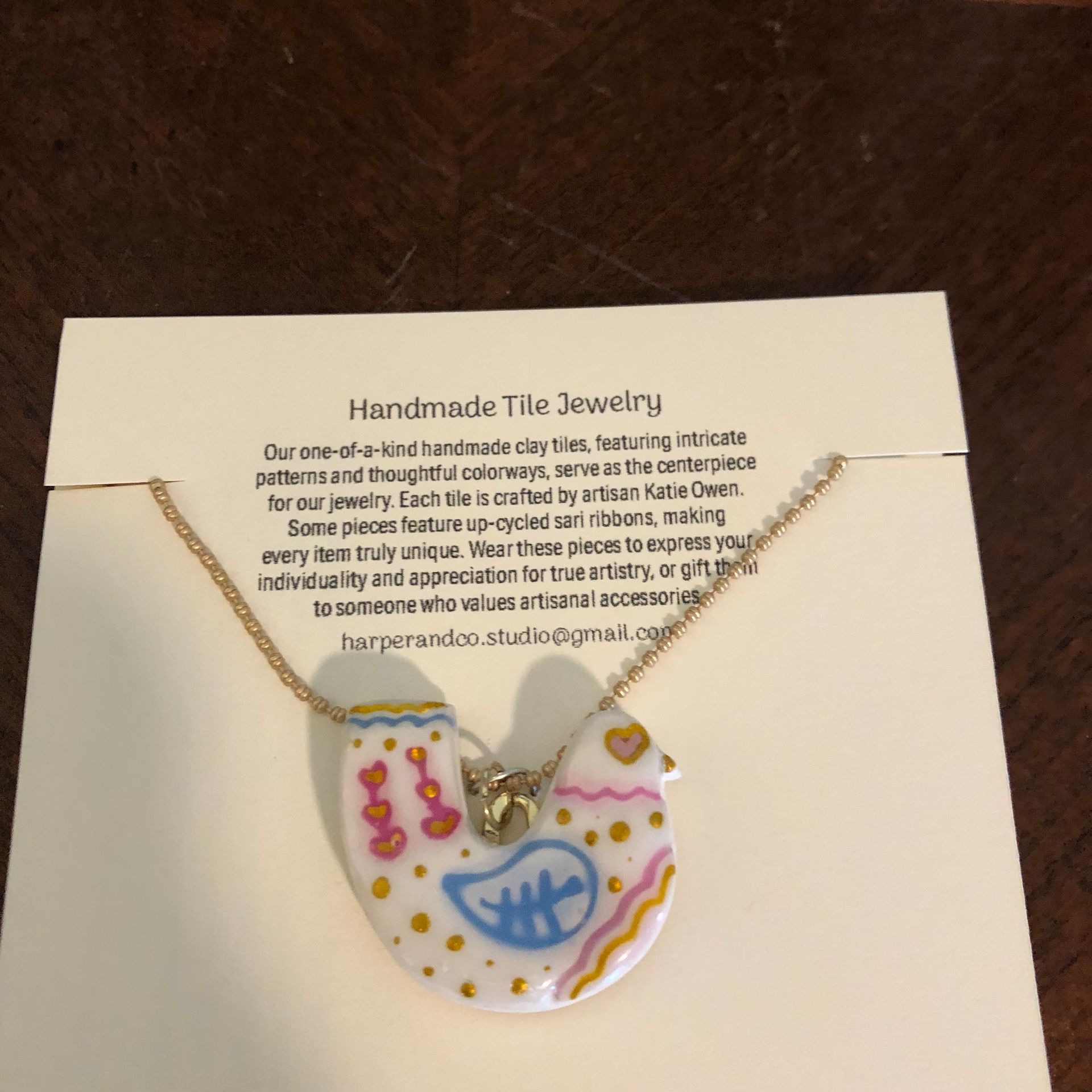 Necklace on a cream card with the brand name Harper & Co, wood table. The pendant has a colorful floral design.