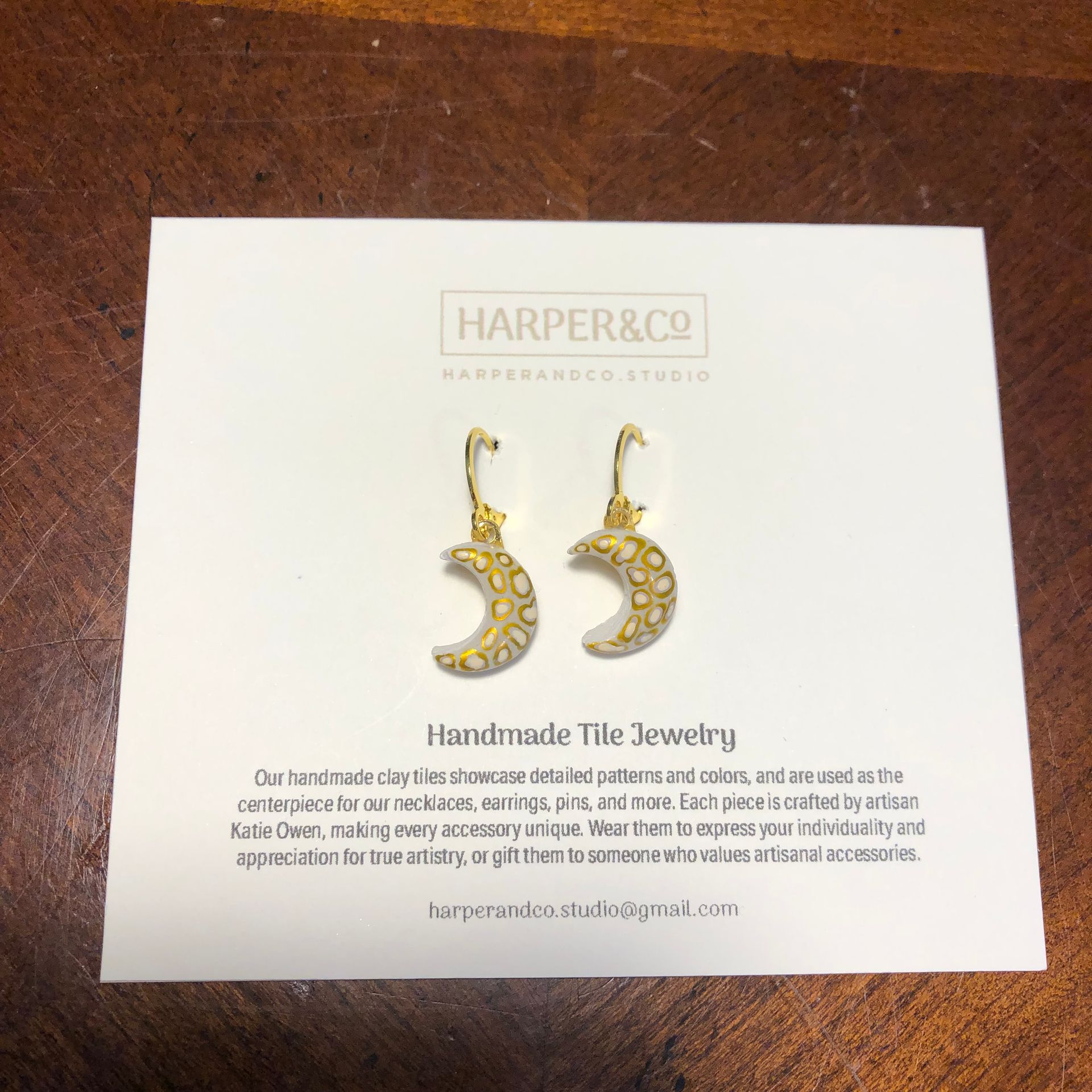 Moon-shaped gold earrings on a white card from Harper & Co. Handmade Tile Jewelry.