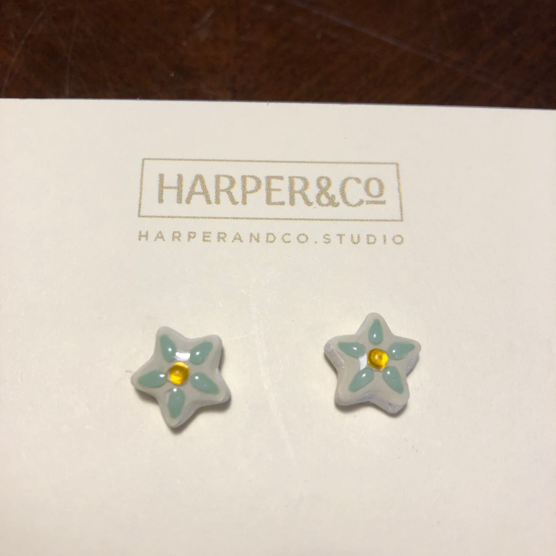 A pair of star-shaped earrings on a white card from Harper & Co. The earrings are light blue with a yellow center.