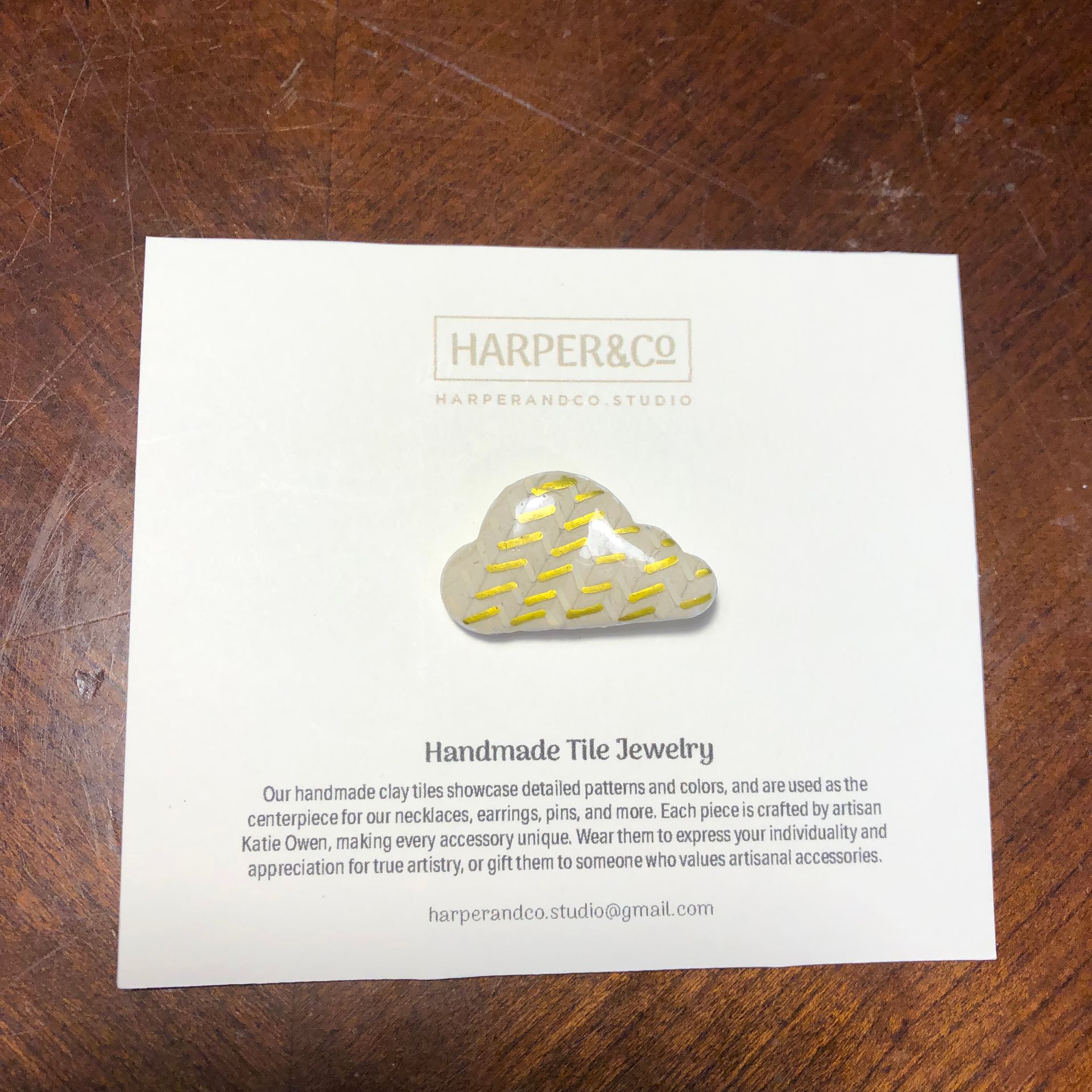 Cloud-shaped handmade tile jewelry pin on a card with logo, text: