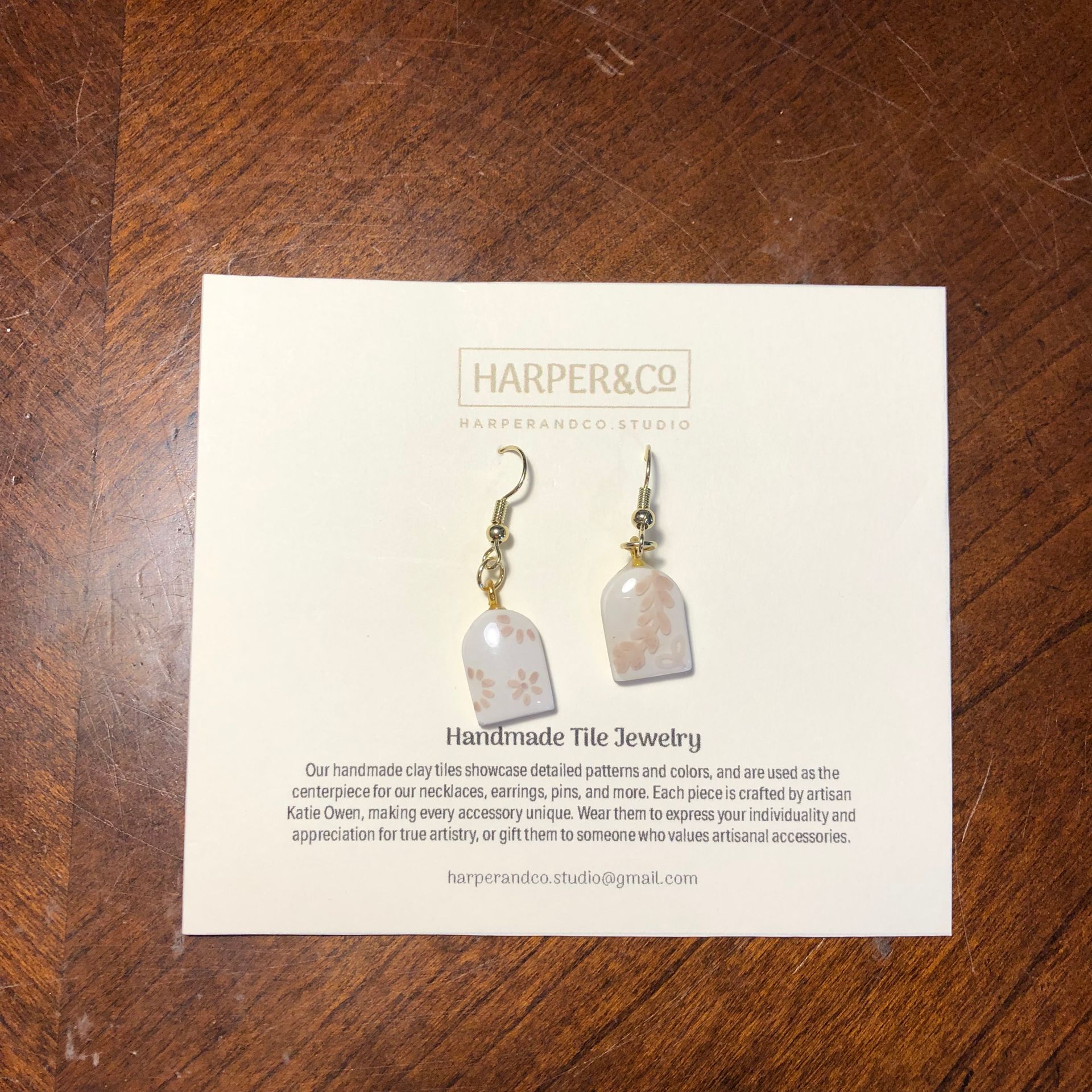 Earrings on a card. Cream-colored with gold accents, dangling from ear hooks.