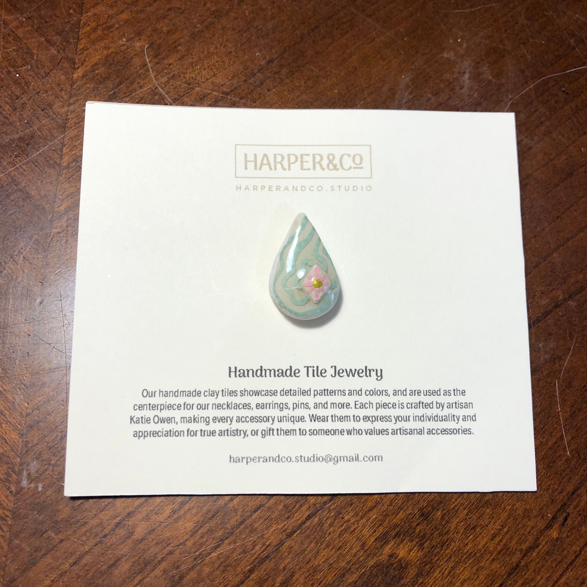 A teardrop-shaped tile pin with pink flower design on a card from Harper & Co. studio.