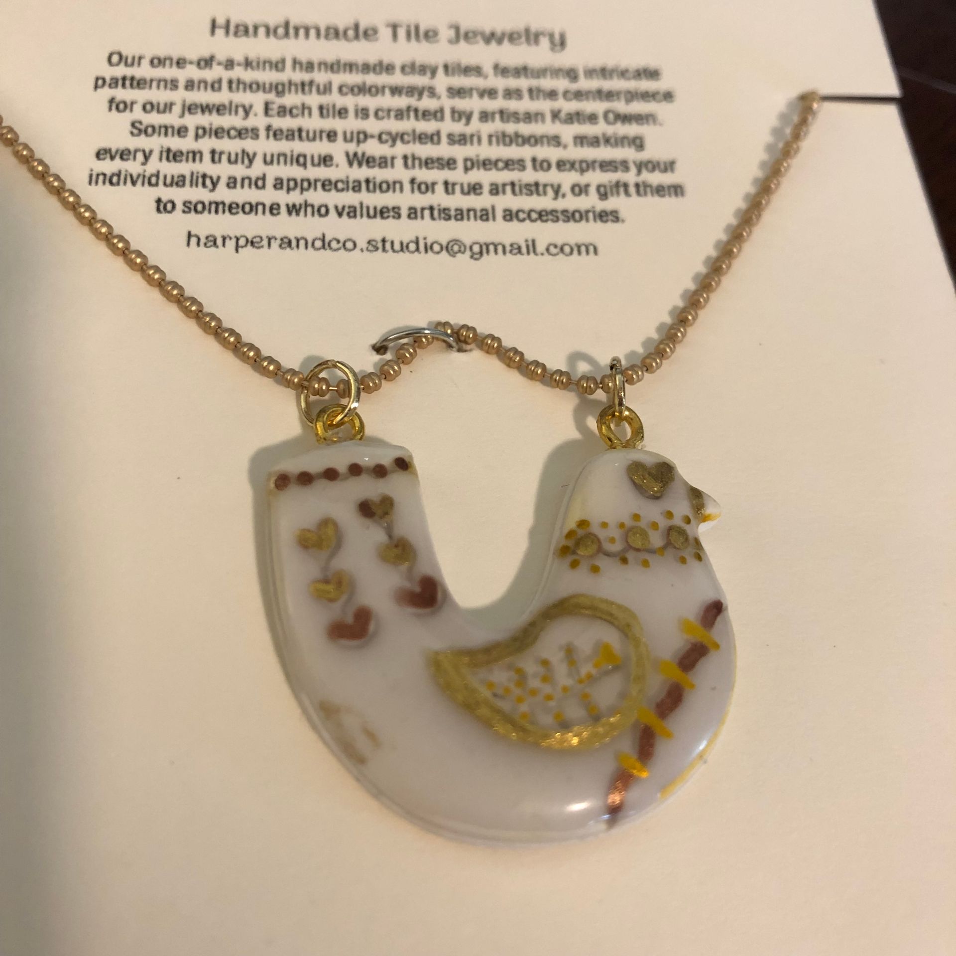 Necklace with white ceramic pendant featuring gold accents on a cream-colored card with text,