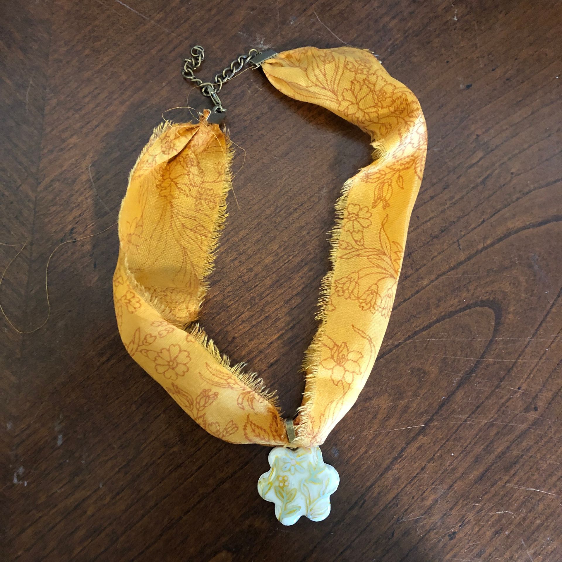 Yellow fabric necklace with a flower pendant on a wooden surface.