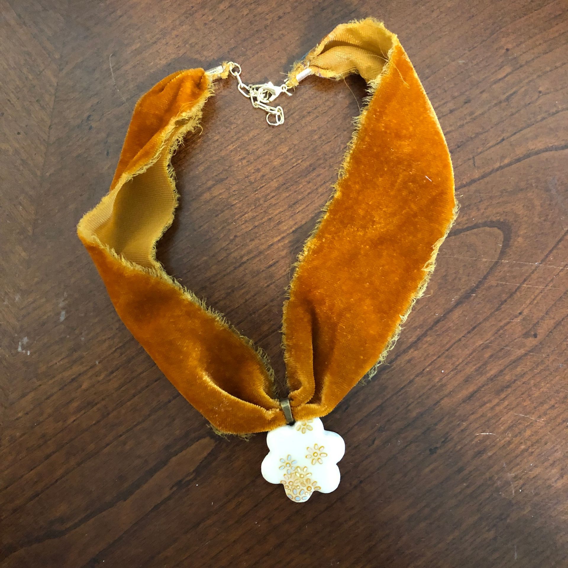 Mustard yellow velvet choker necklace with white flower pendant, on wood table.