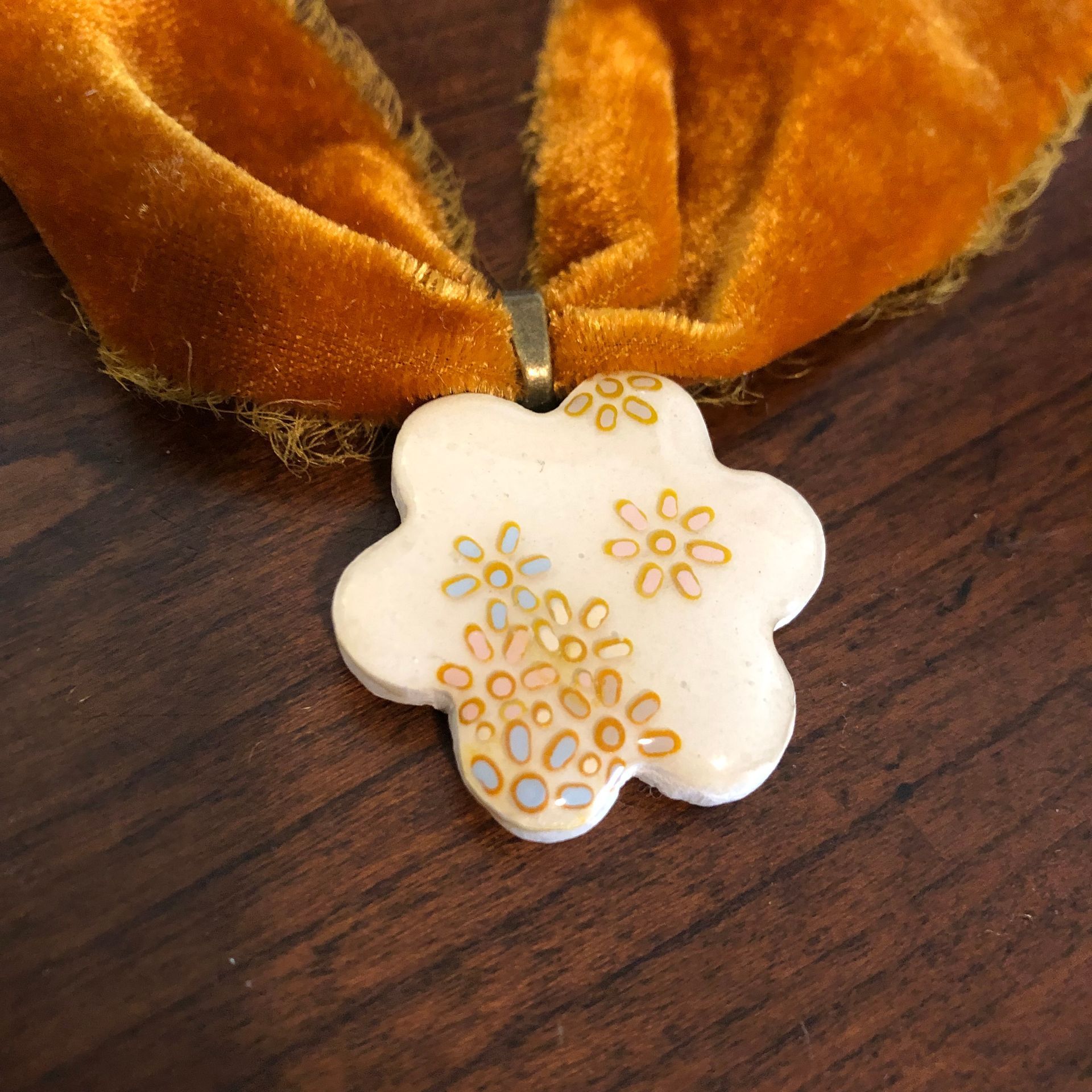 Mustard yellow velvet choker necklace with white flower pendant, on wood table.
