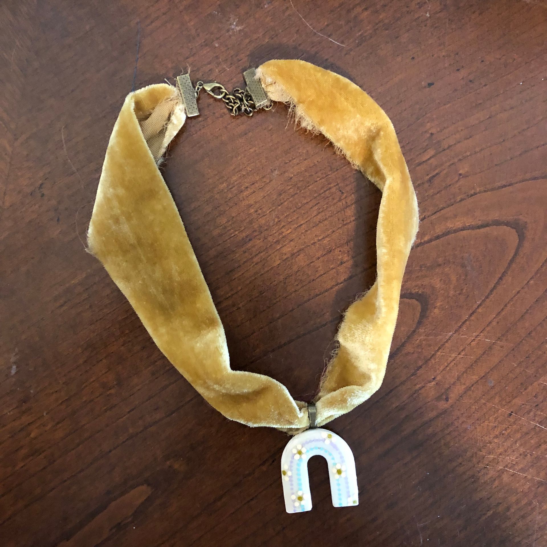Mustard-yellow velvet choker necklace with a rainbow pendant on a wooden surface.