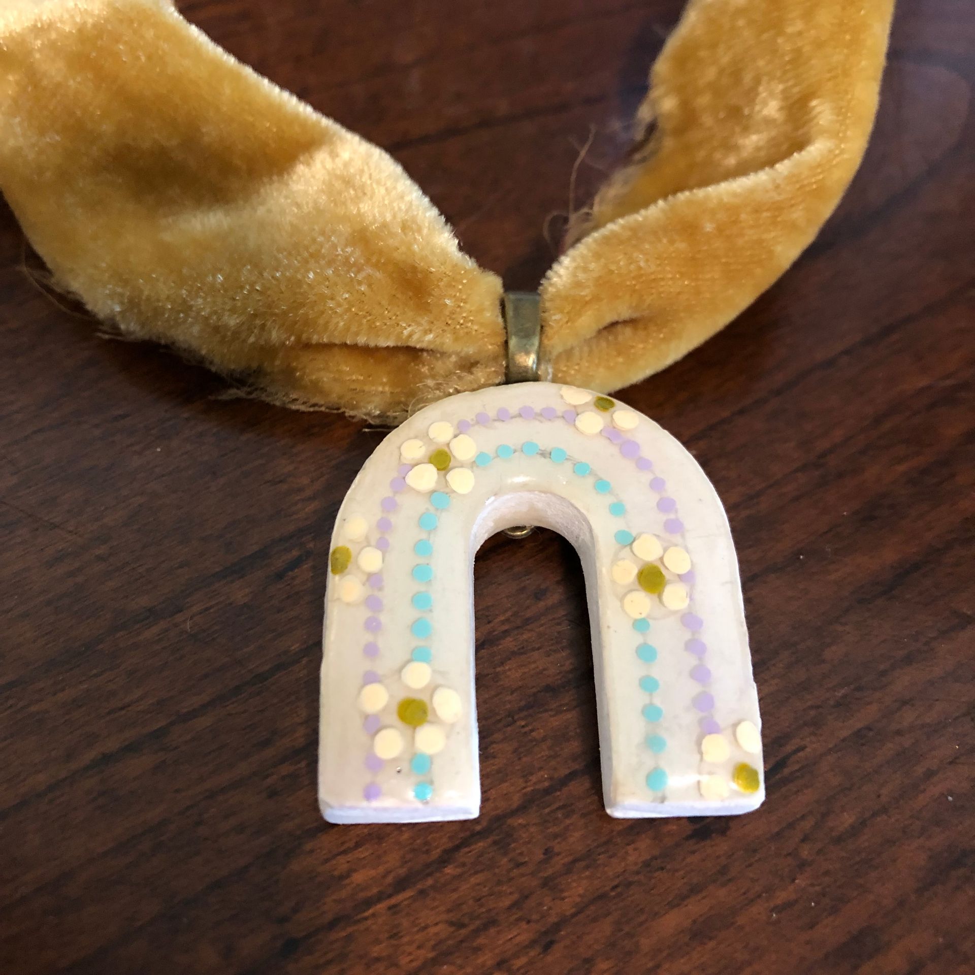 Mustard-yellow velvet choker necklace with a rainbow pendant on a wooden surface.