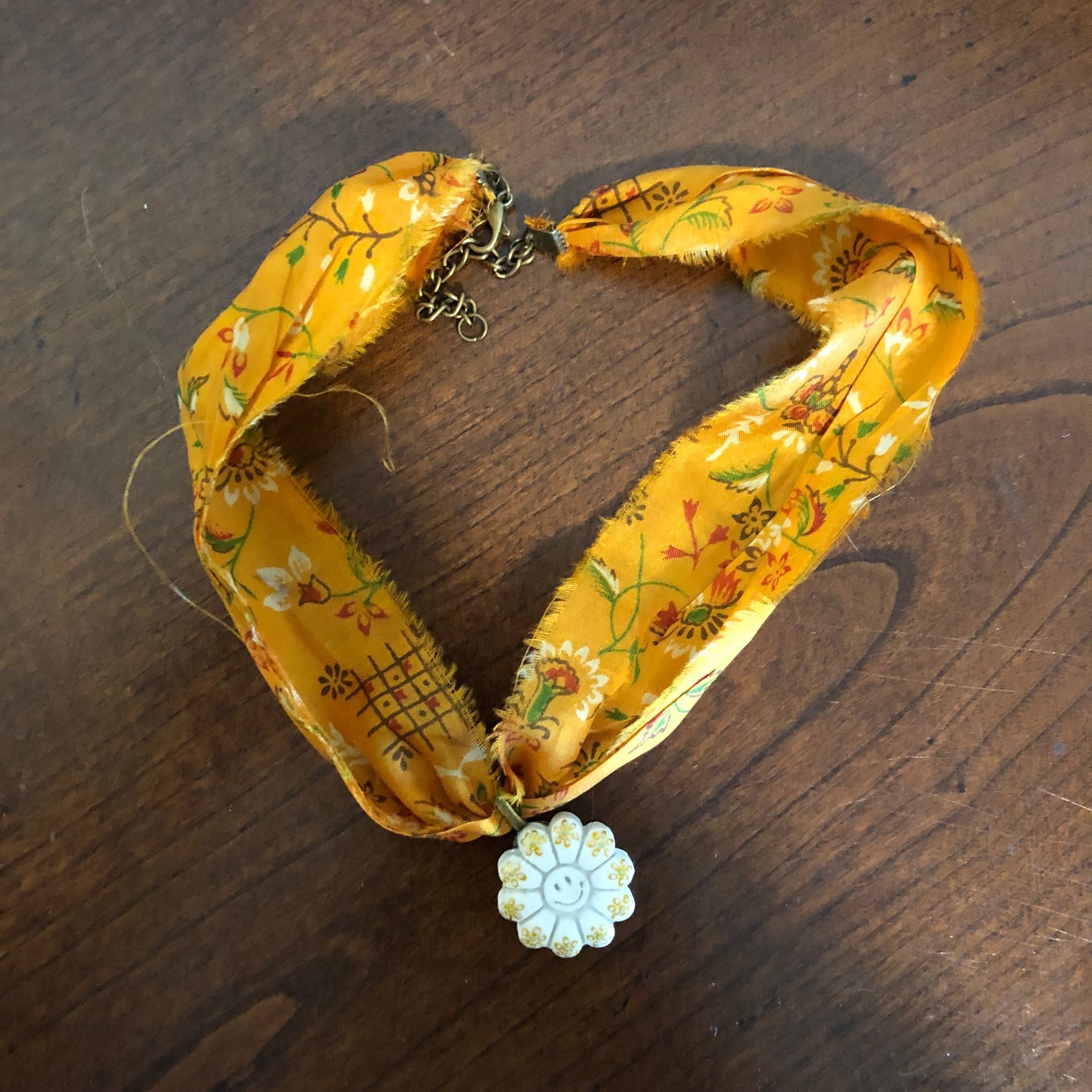 Yellow floral fabric necklace with a white flower pendant on a wood surface.