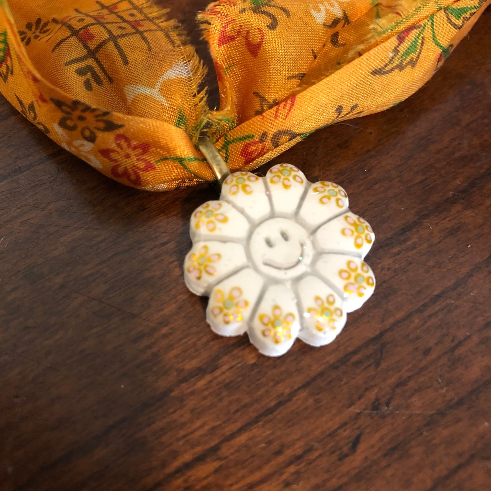 Yellow floral fabric necklace with a white flower pendant on a wood surface.